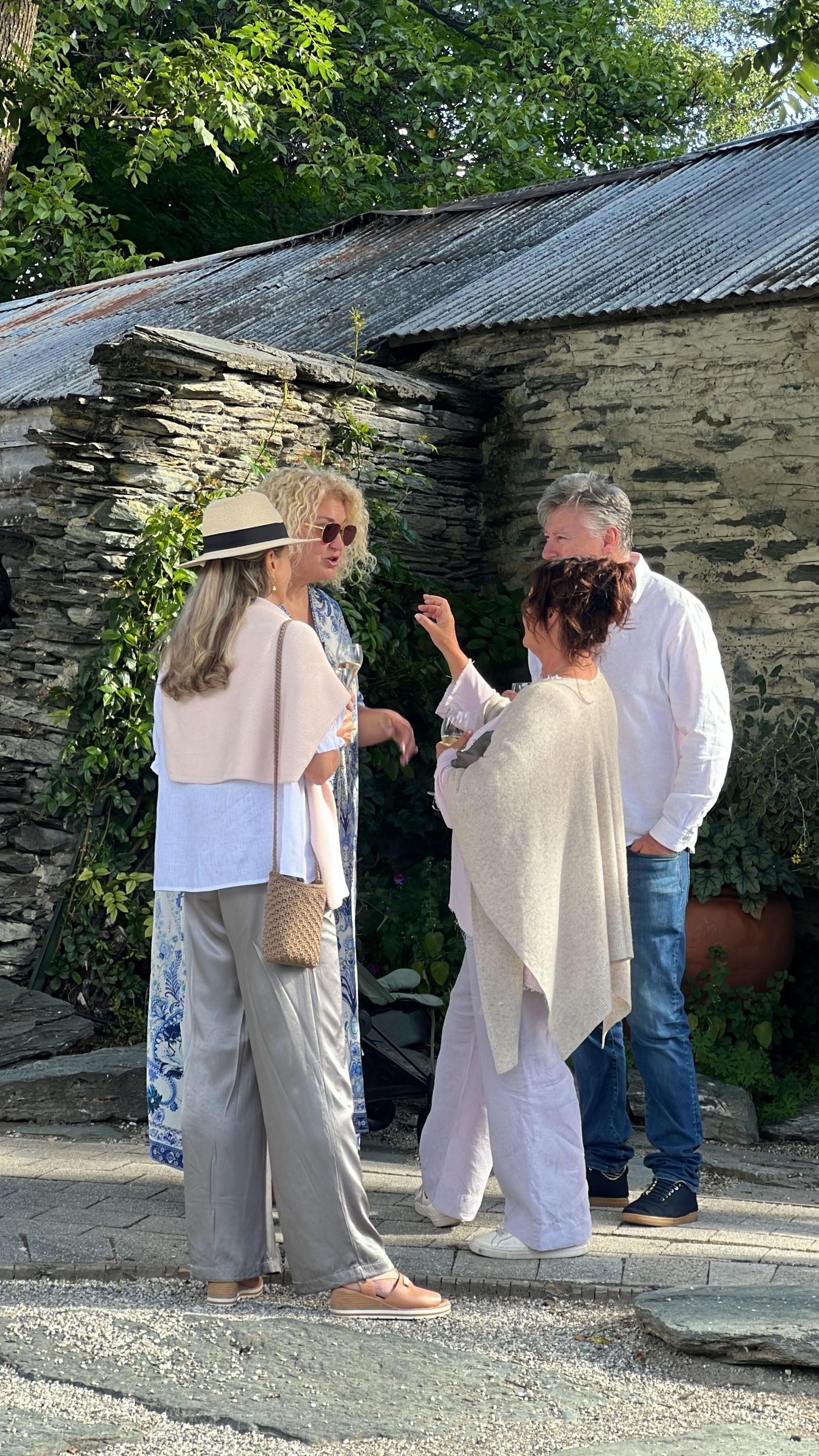 People gathering outside a rustic stone building on a sunny day.