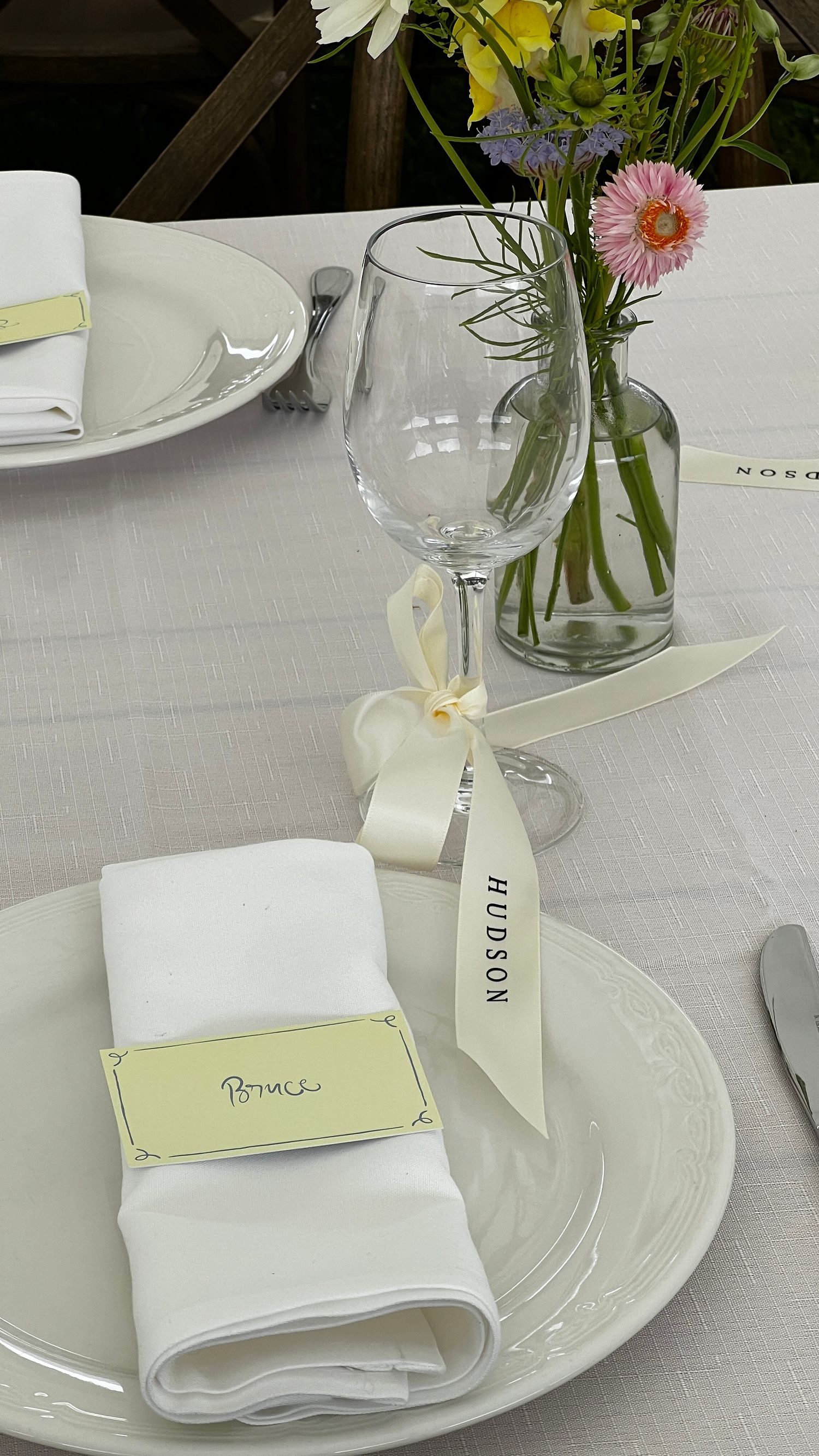 Elegant table setting with white linens, place cards, and delicate floral centerpieces.