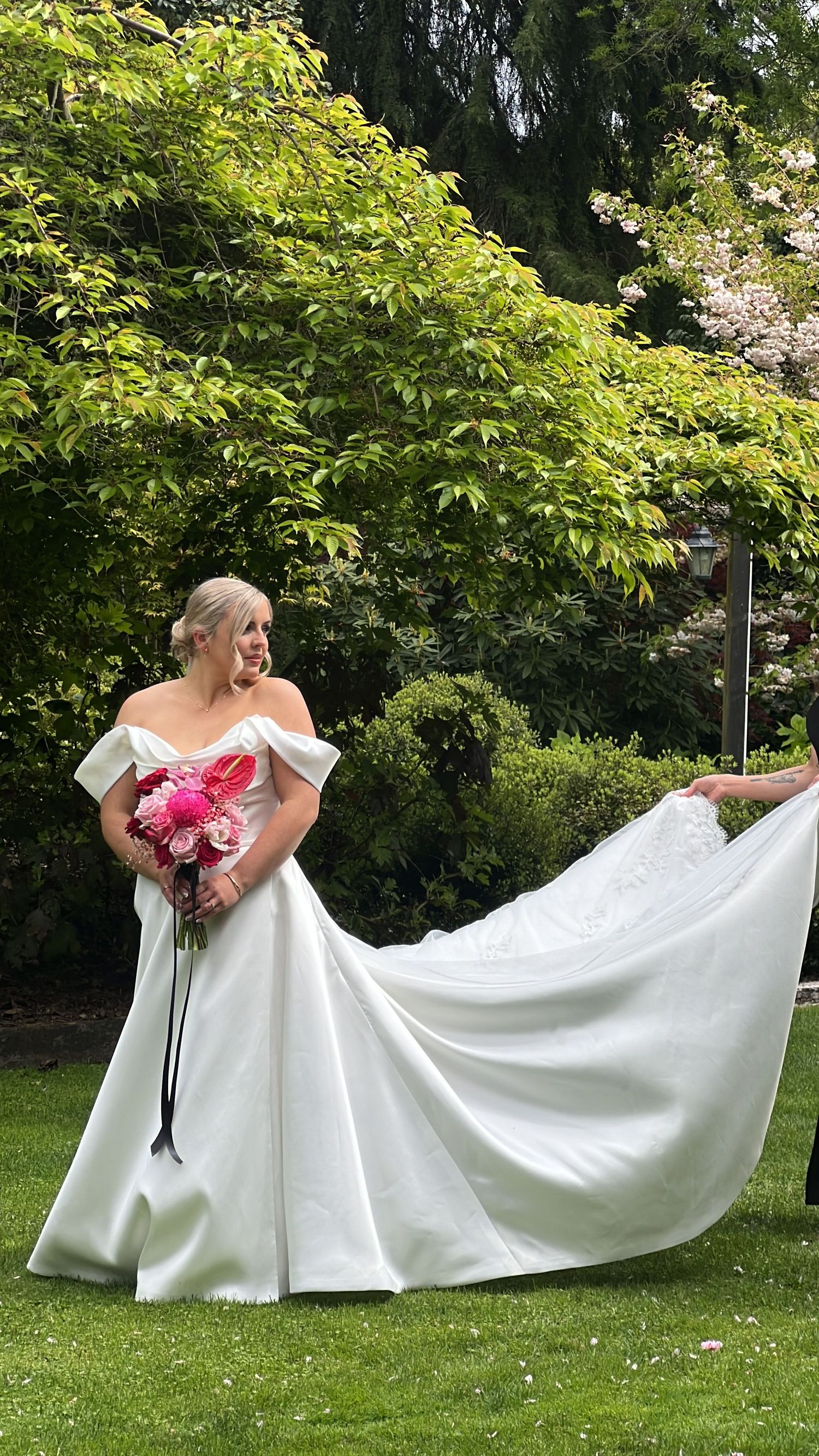 White wedding dress spreads across green lawn in garden setting.