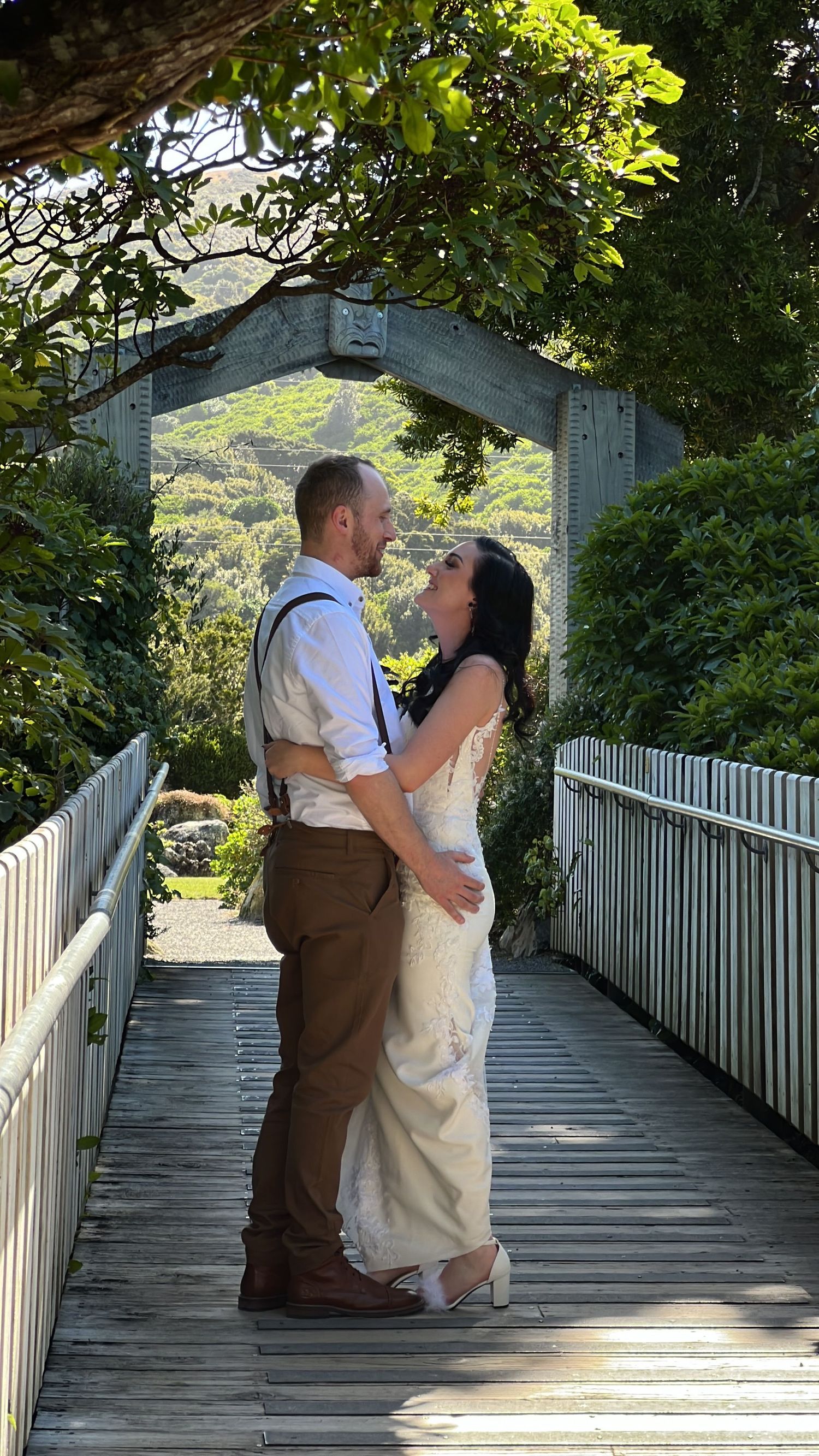 A couple shares an intimate moment on a wooden bridge surrounded by lush greenery.