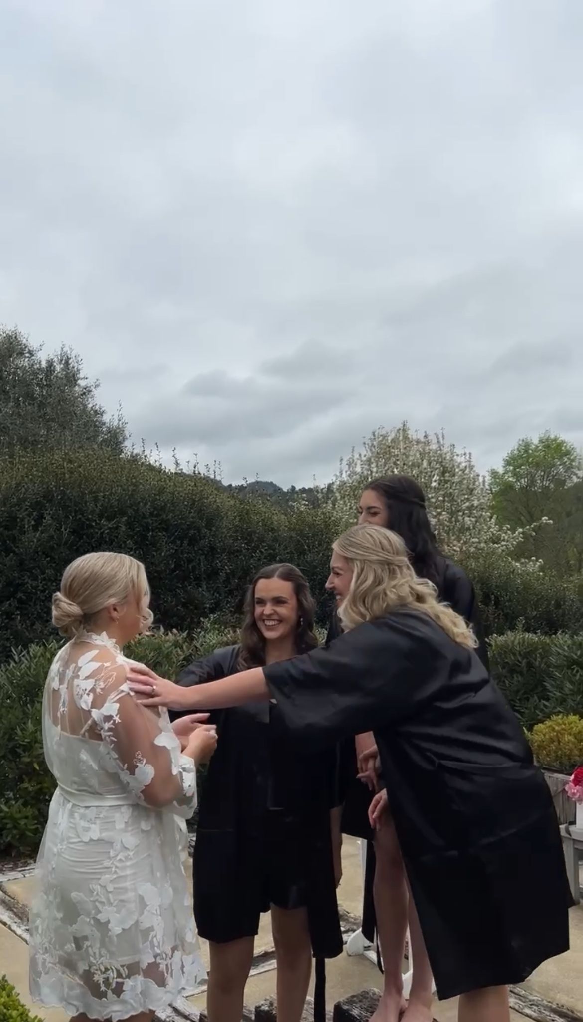 Wedding party in black dresses and white gown celebrating outdoors.