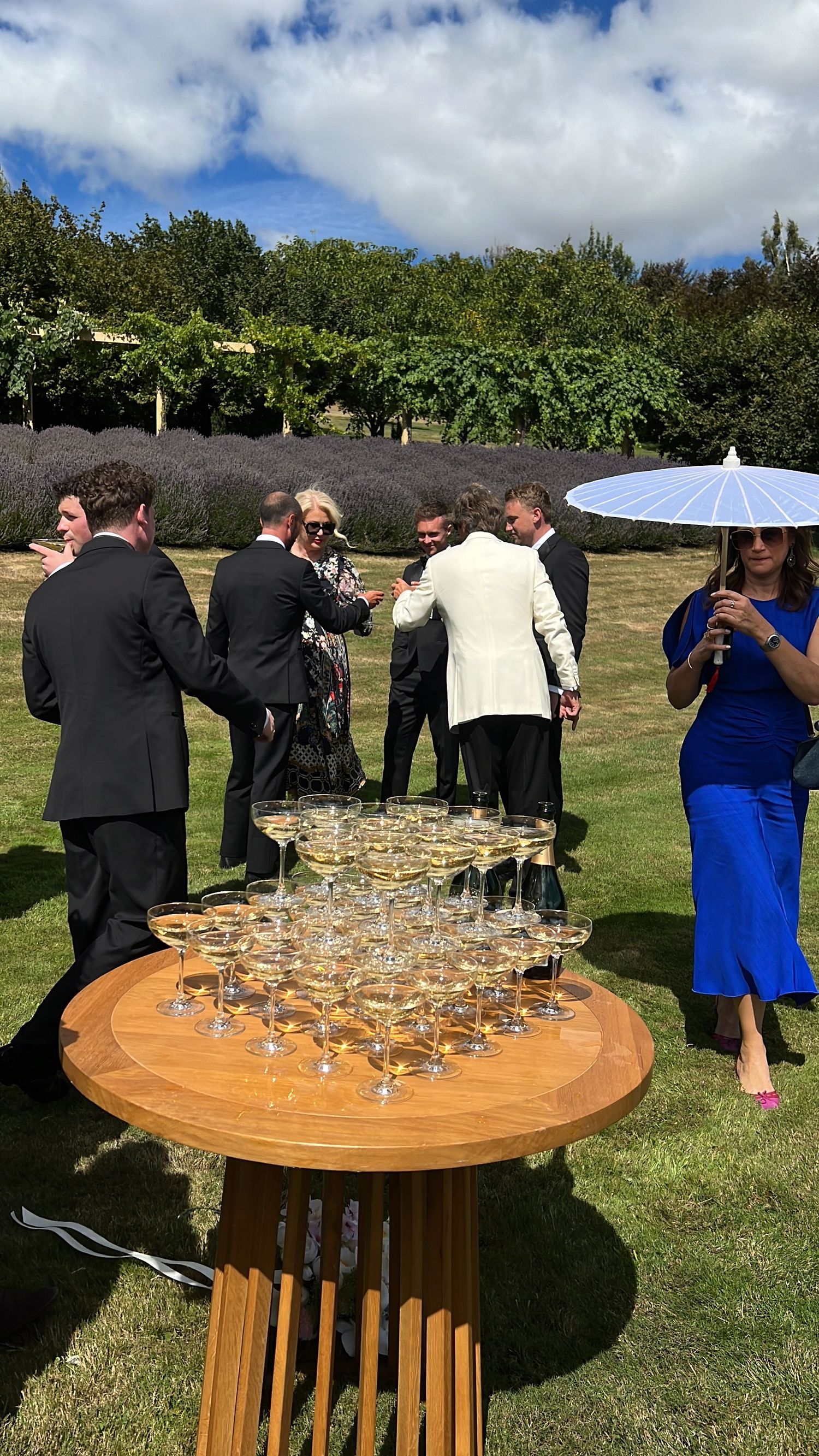 Wedding guests gathered around a circular wooden table with champagne glasses at an outdoor reception. content creation in new zealand