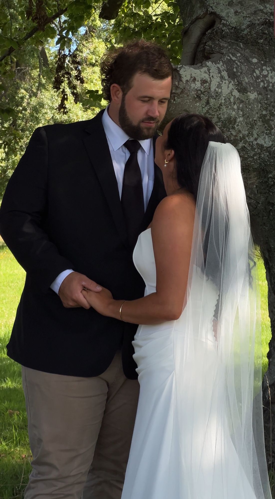A couple shares an intimate moment in a garden setting during their wedding, with the bride wearing a flowing white dress and veil.