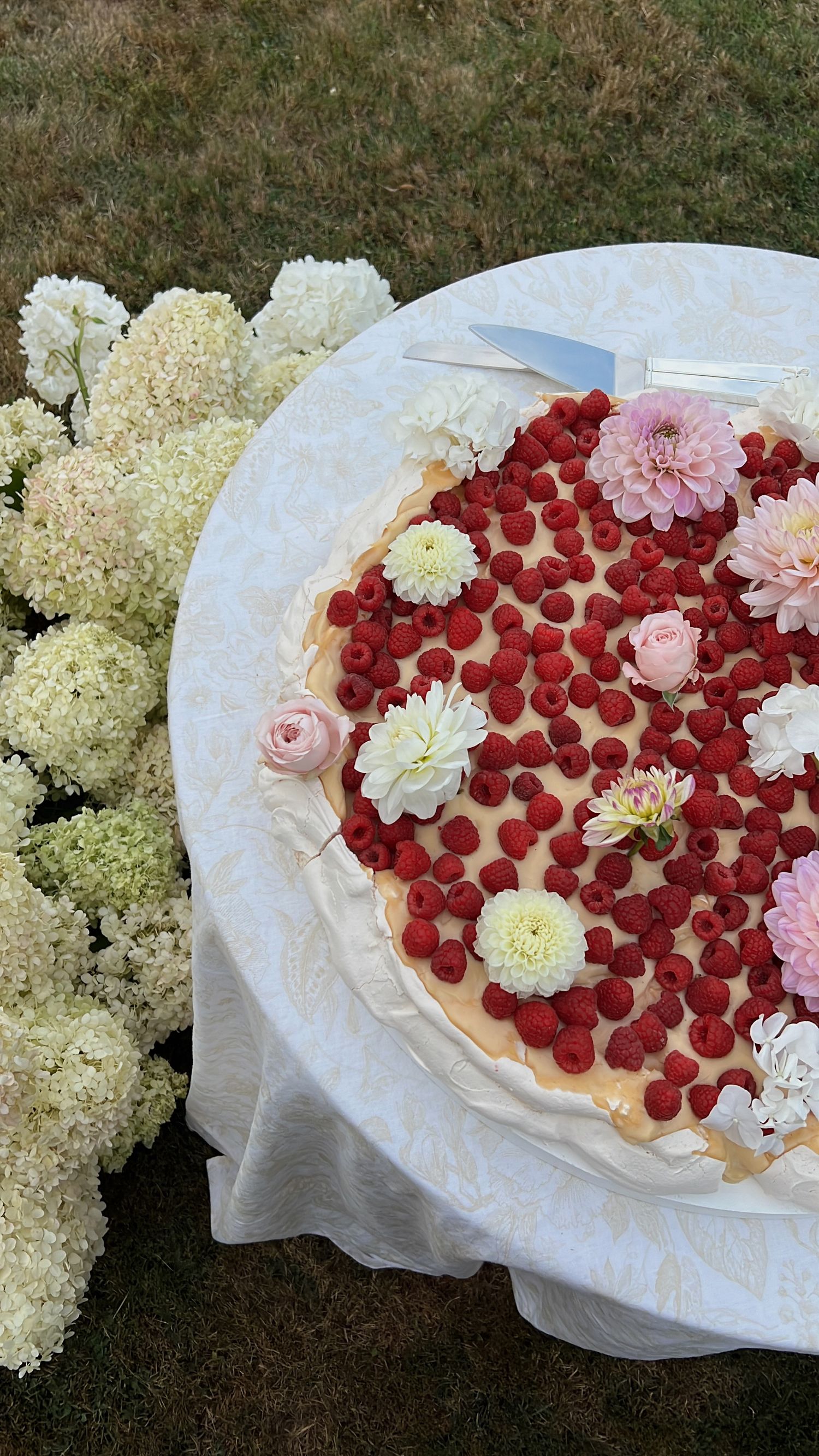 Heart-shaped dessert decorated with fresh raspberries and white flowers on a white tablecloth.