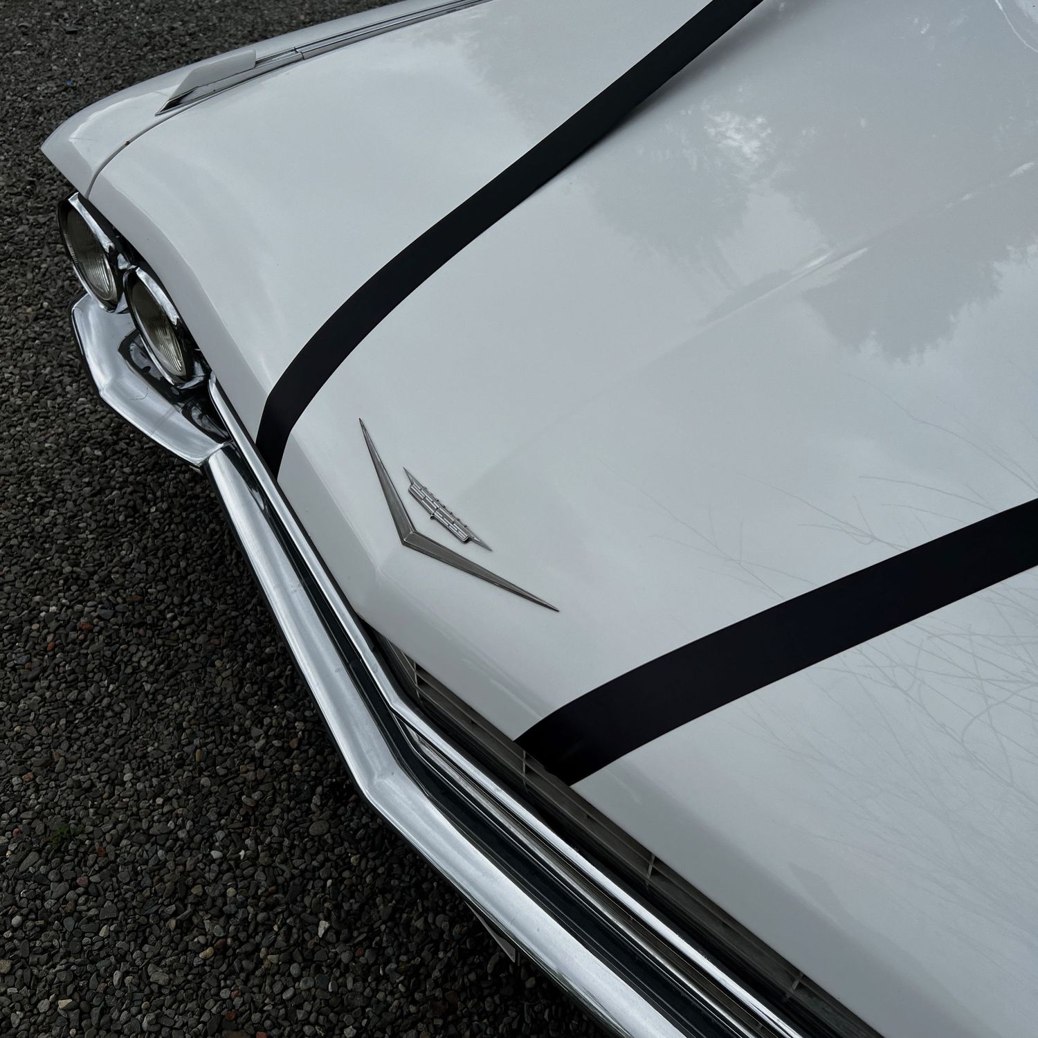 Close up detail of a white vintage car's hood and fender showing sleek chrome trim.