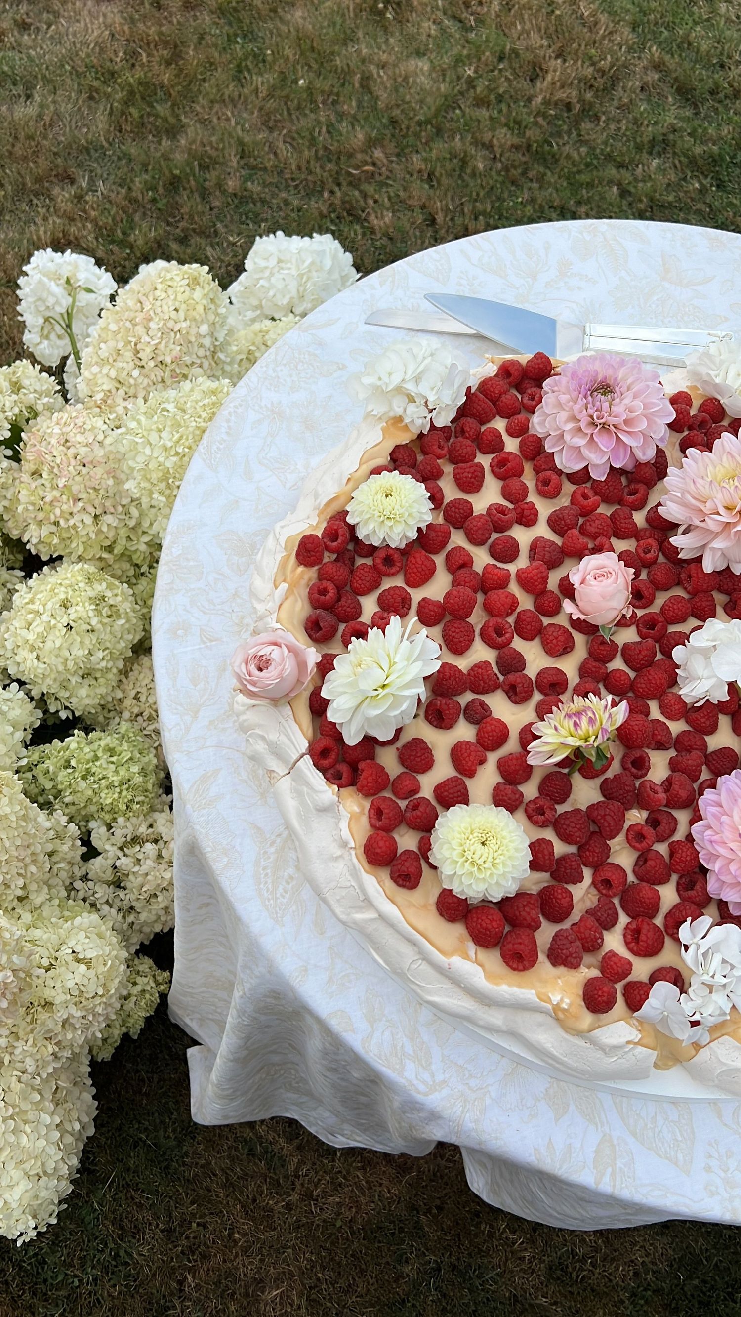 Wedding cake decorated with red raspberries, pink roses, and white flowers on a delicate lace tablecloth.content creation in new zealand
