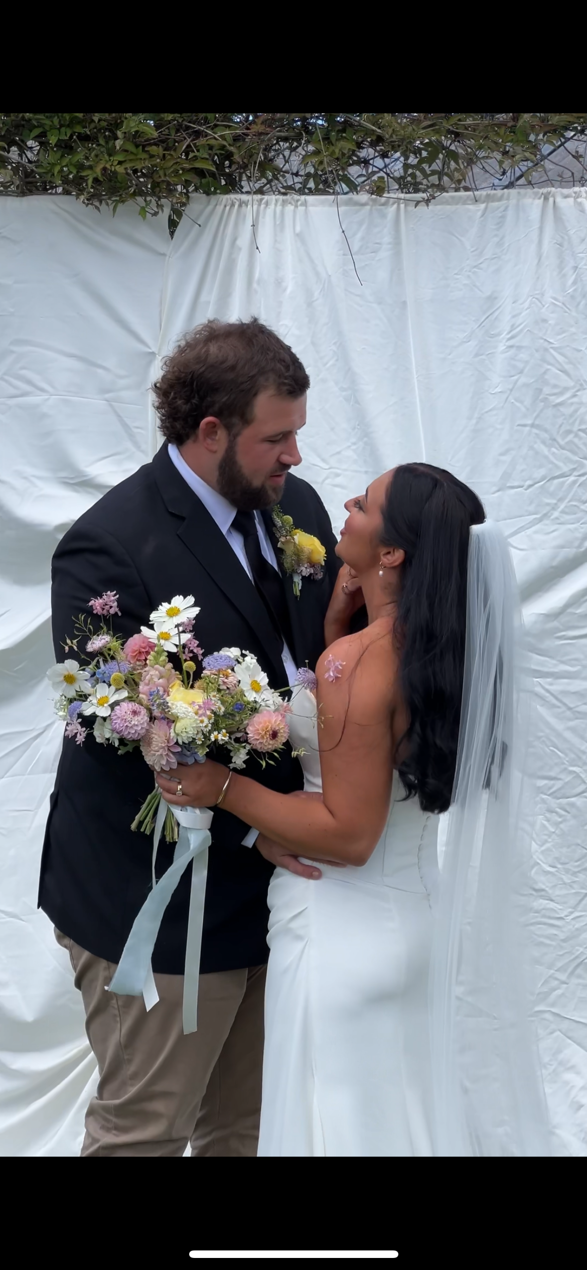 Wedding couple sharing intimate moment against white backdrop with spring flower bouquet.