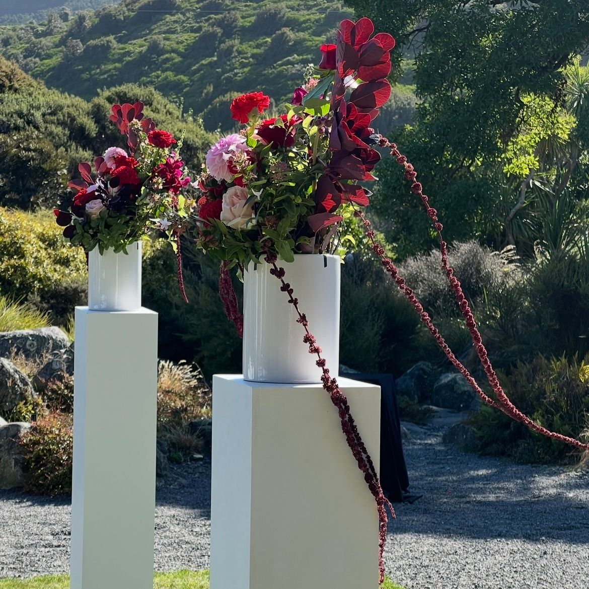 Decorative white pedestals with cascading red bougainvillea flowers against a mountainous landscape backdrop.