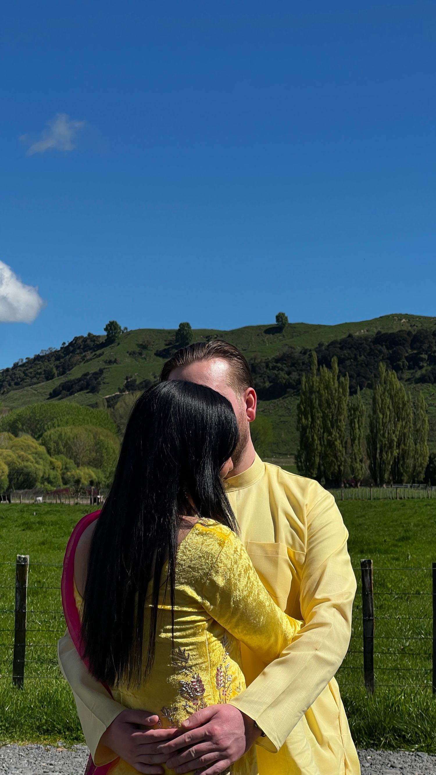 Couple in matching yellow outfits embracing in front of rolling green hills.