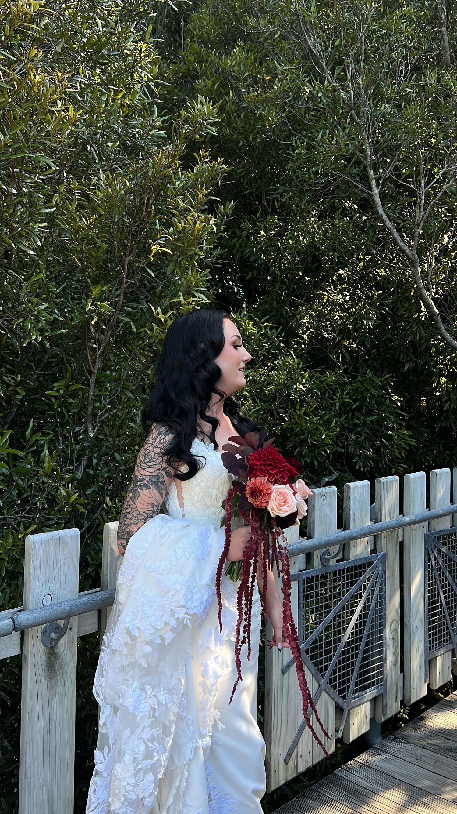 A figure in a flowing white dress stands on a wooden bridge surrounded by lush greenery.