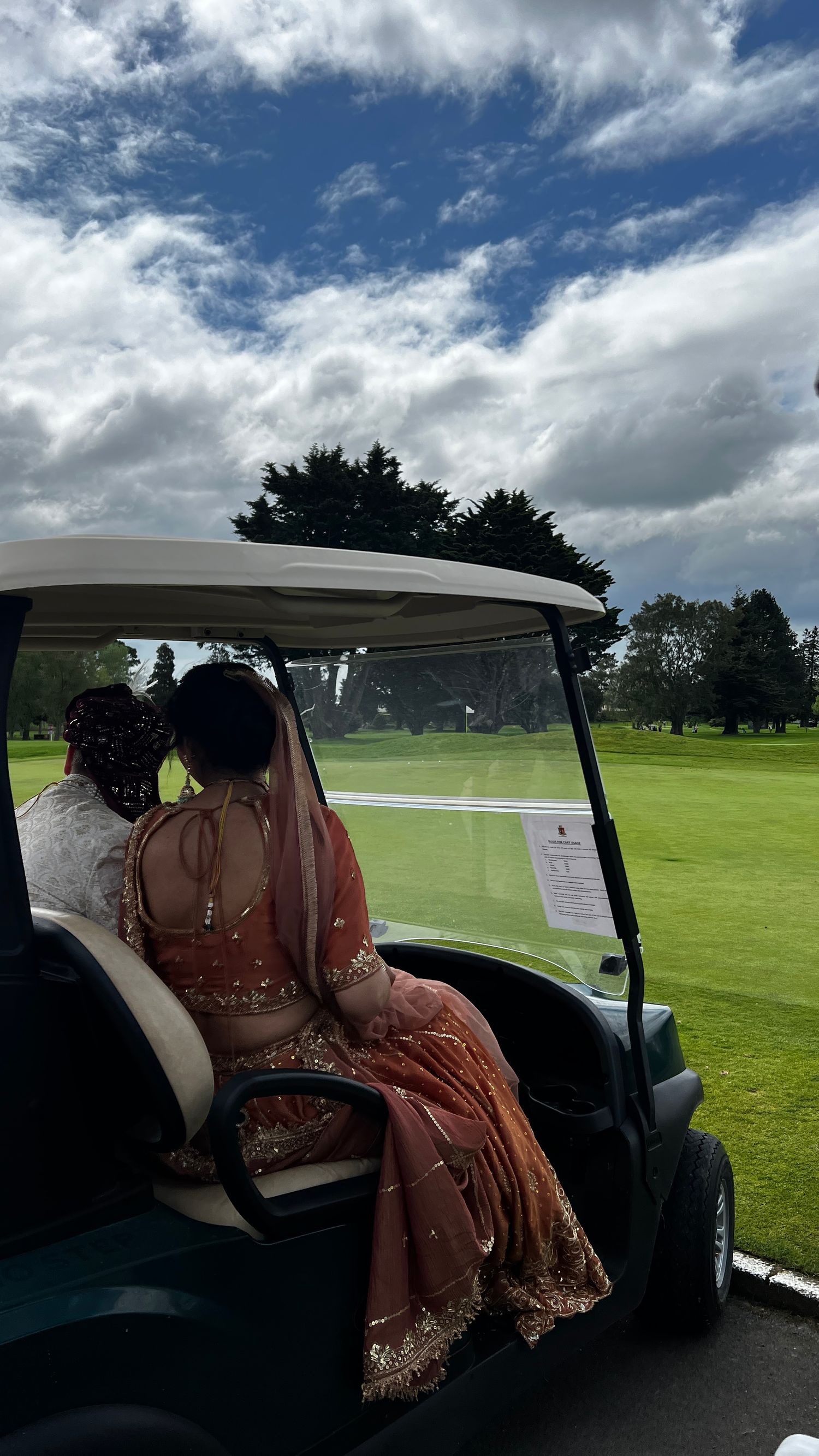 Golf cart ride across a green course under cloudy skies with traditional Indian attire visible.