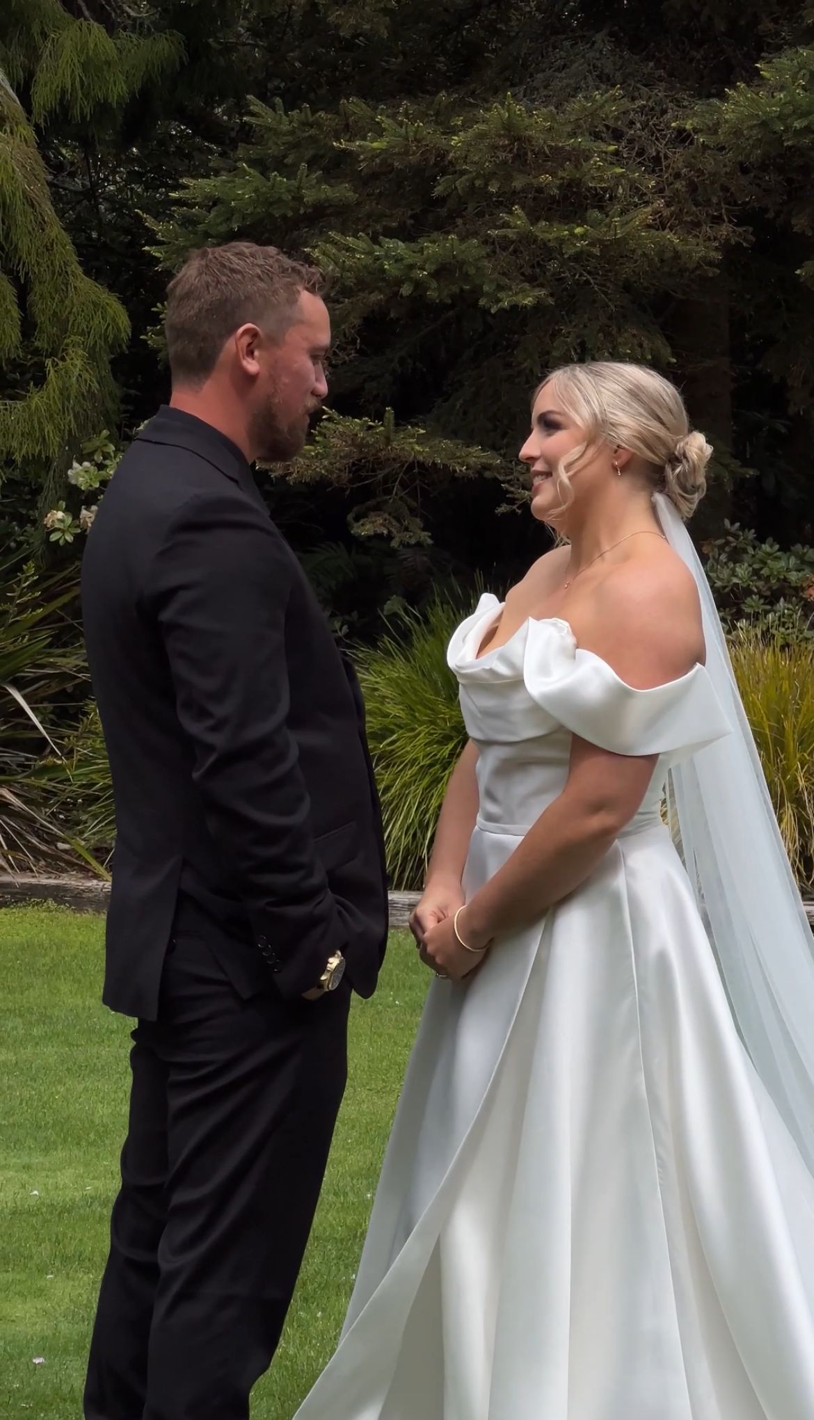 Wedding couple sharing a moment in elegant white gown and black suit on garden grounds.