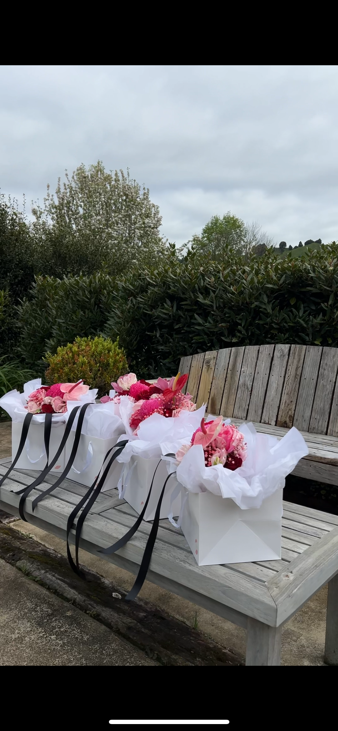 White gift bags with pink flowers arranged on wooden bench.