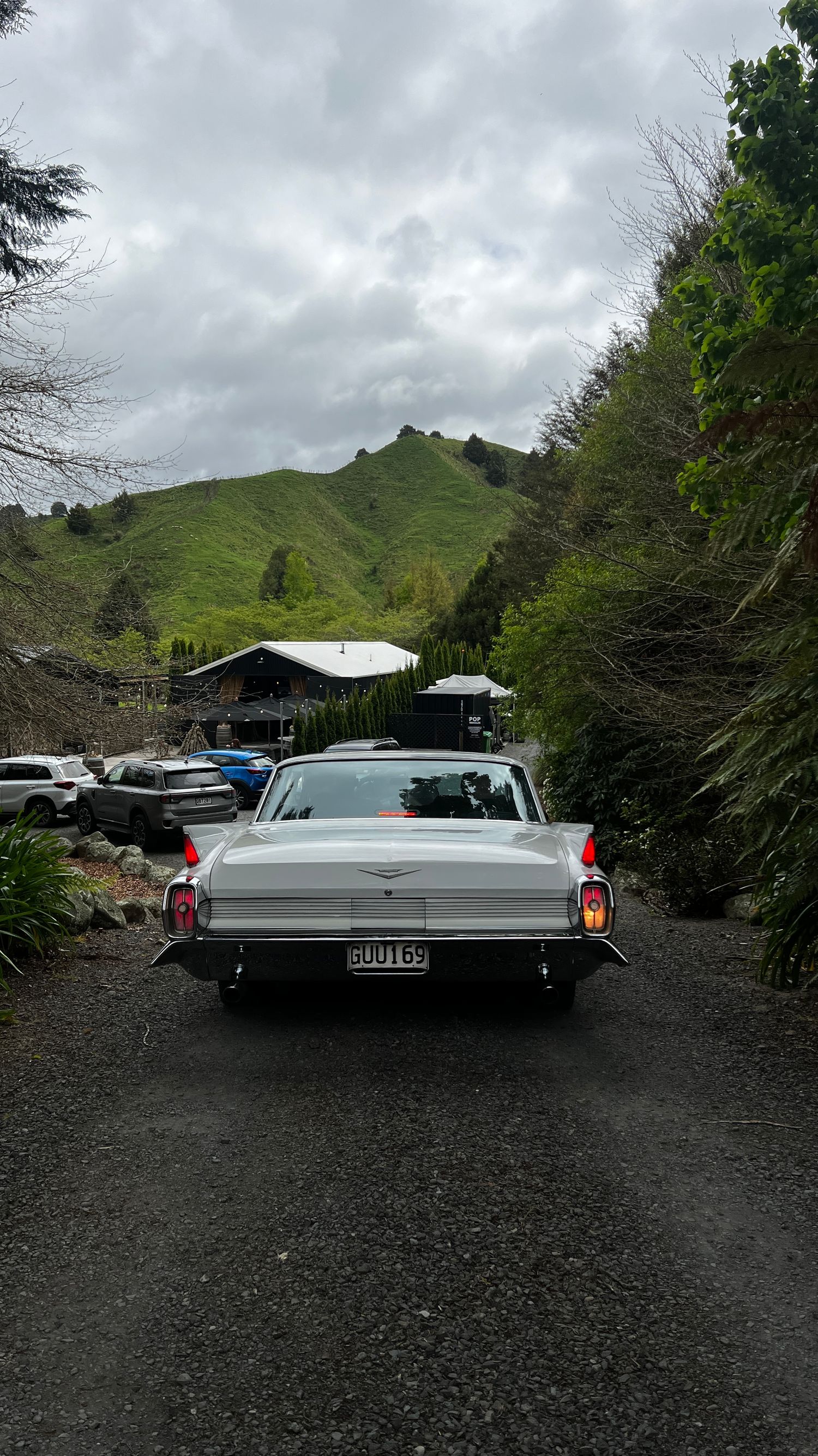 Classic white vintage car parked against backdrop of green hills and cloudy sky.