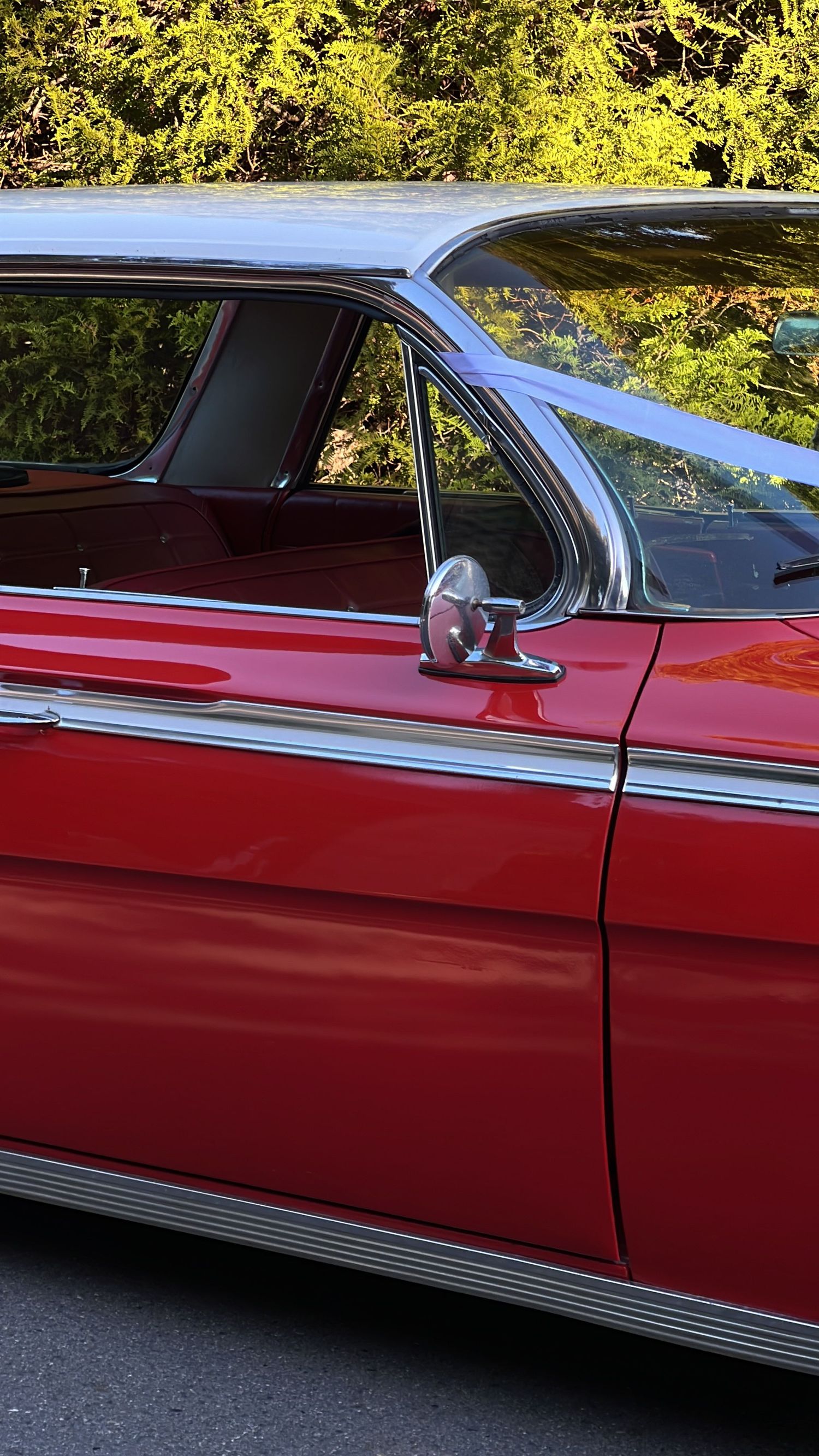 Side view of a classic red and chrome vintage car parked outdoors.