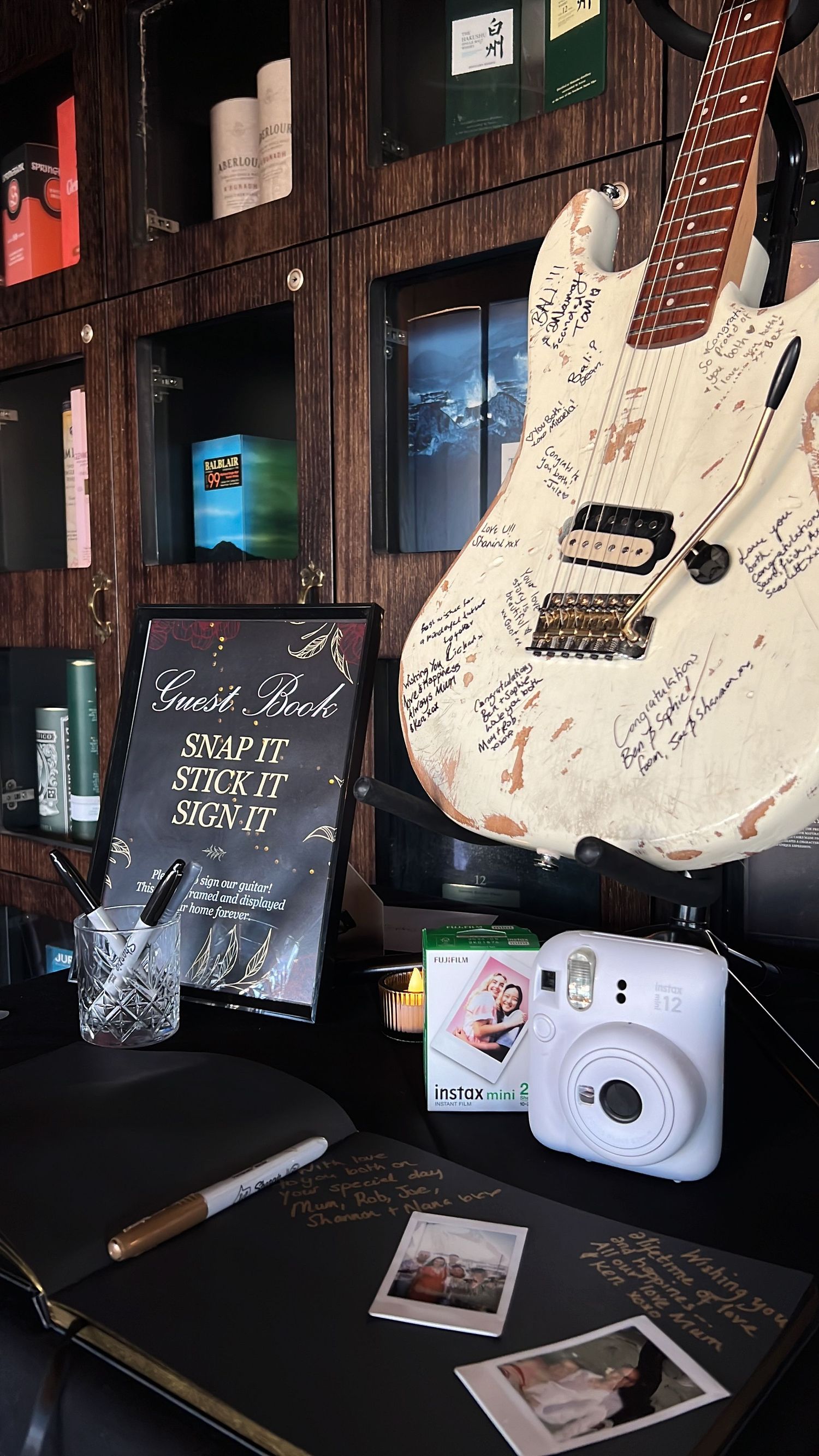 White electric guitar with signatures displayed next to a polaroid camera and books.
