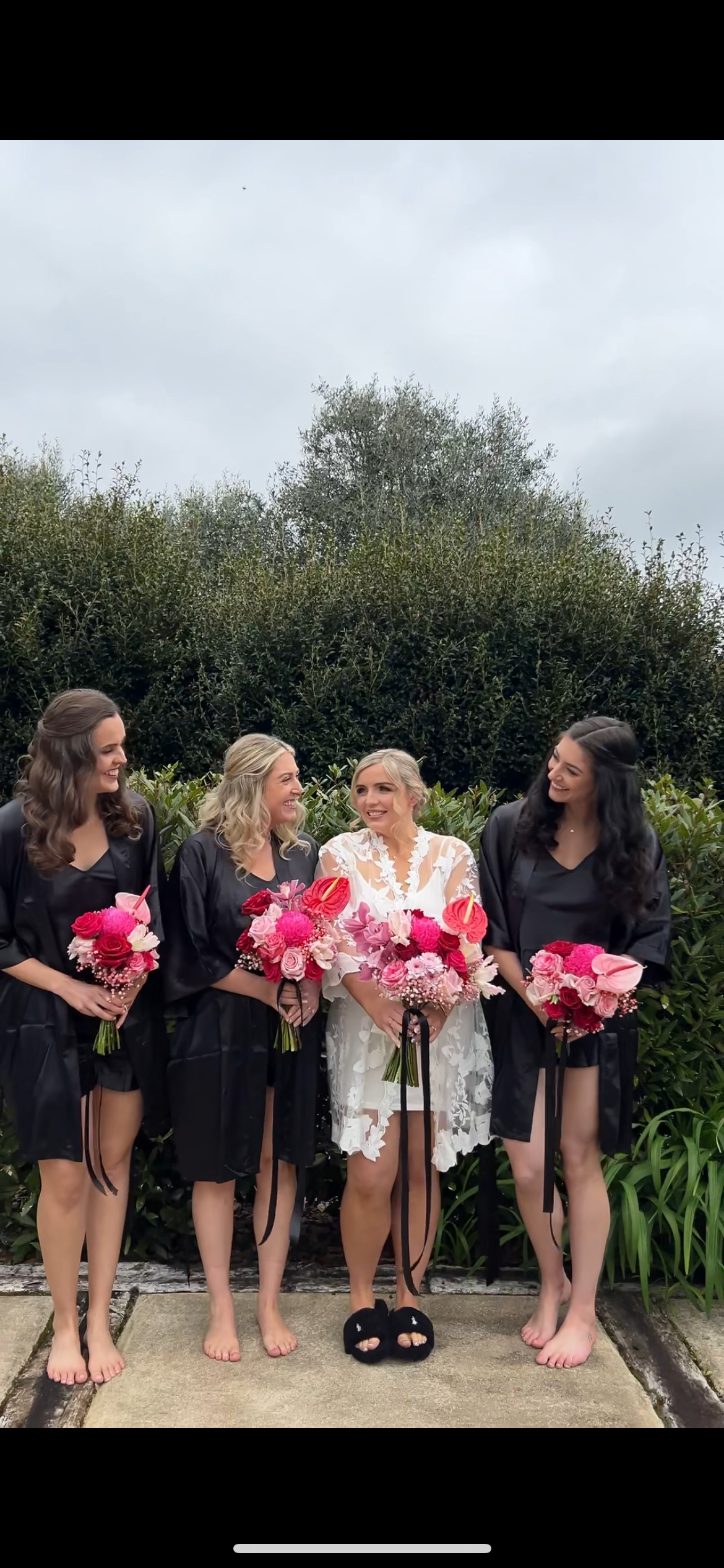Wedding party poses barefoot on garden wall holding pink bouquets.