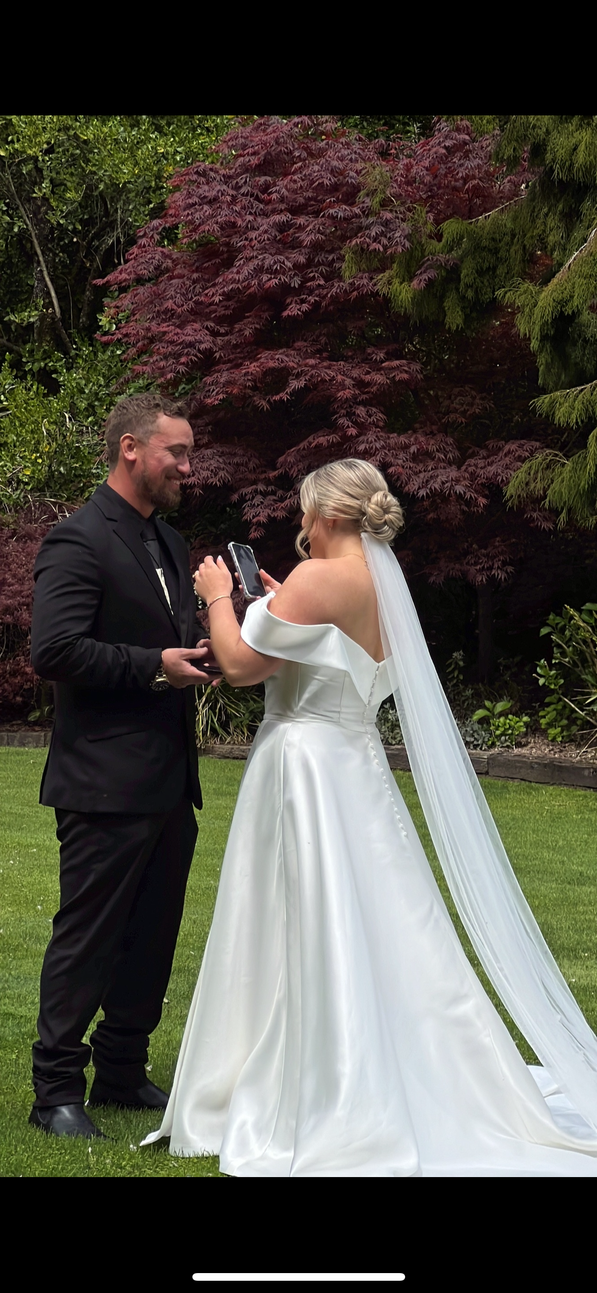 A wedding ceremony takes place outdoors with a beautiful burgundy Japanese maple tree in the background.