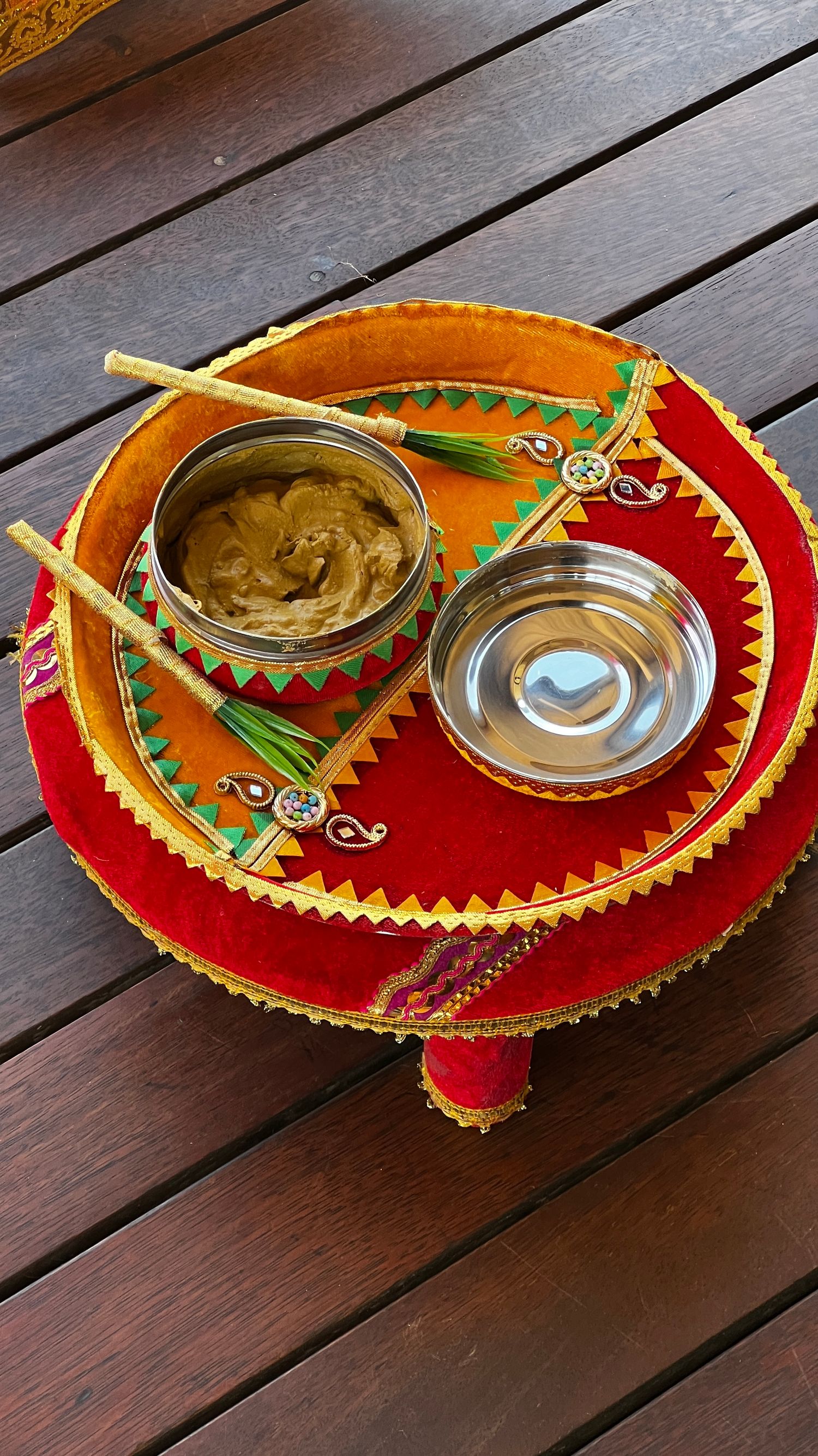 Decorative red and gold low table with traditional Indian henna paste and water bowls on wooden deck.indian wedding