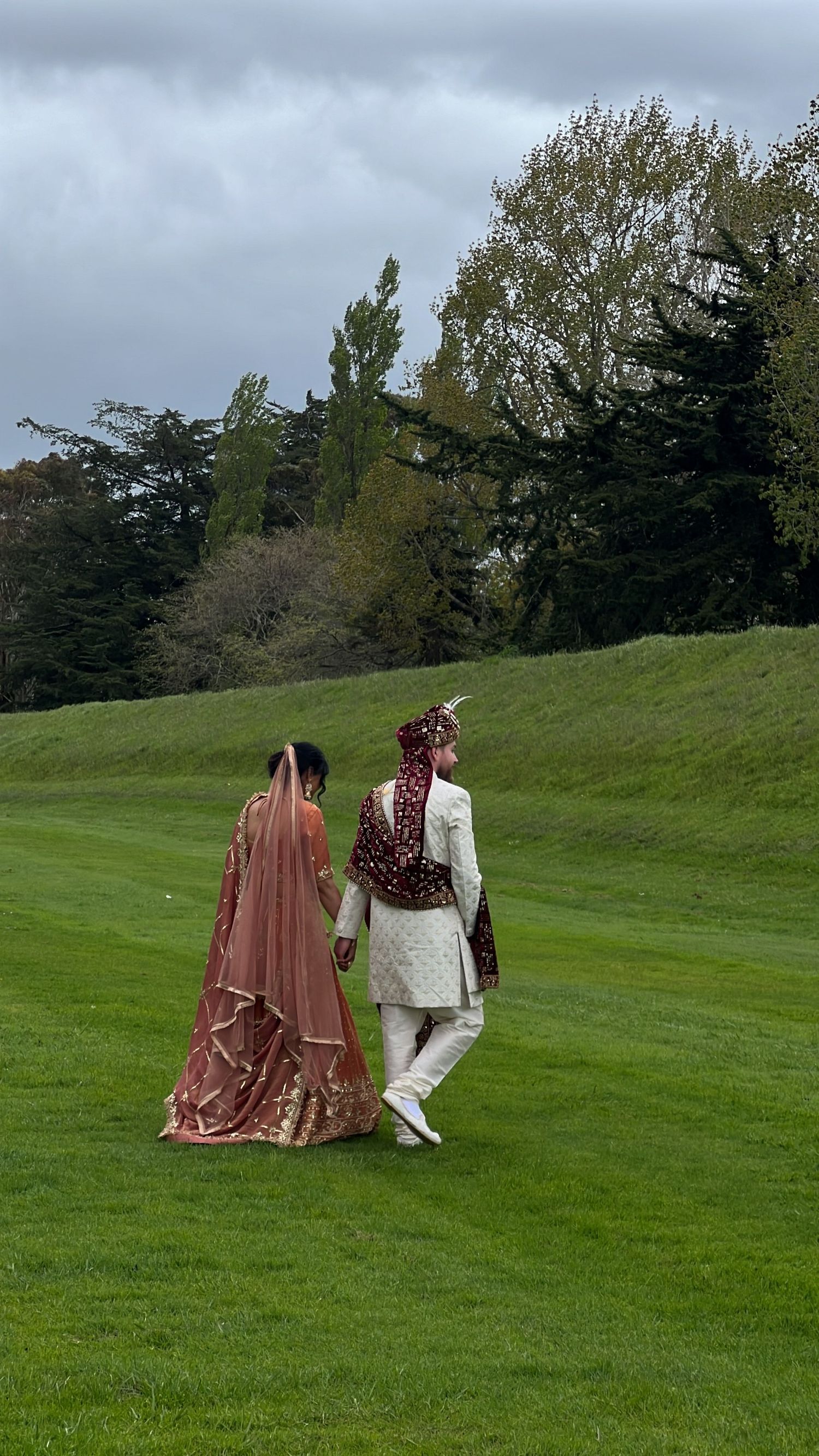 Couple in traditional Indian wedding attire photographed on a lush green hillside.