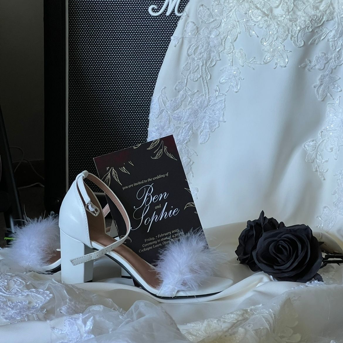 Elegant white wedding shoe with feather detail displayed alongside a black rose and bridal accessories.