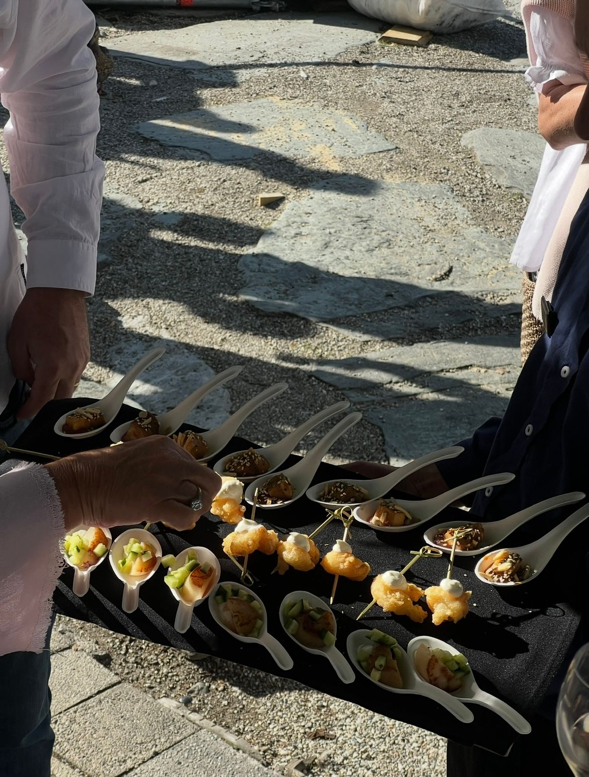 Black plates arranged on a stone surface display appetizer portions of gourmet food and garnishes.