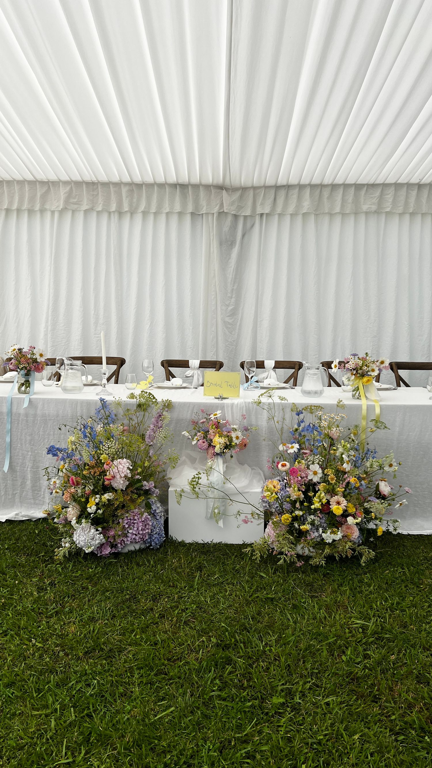 White tent reception setup with floral arrangements lining the base of the walls.content creation in new zealand