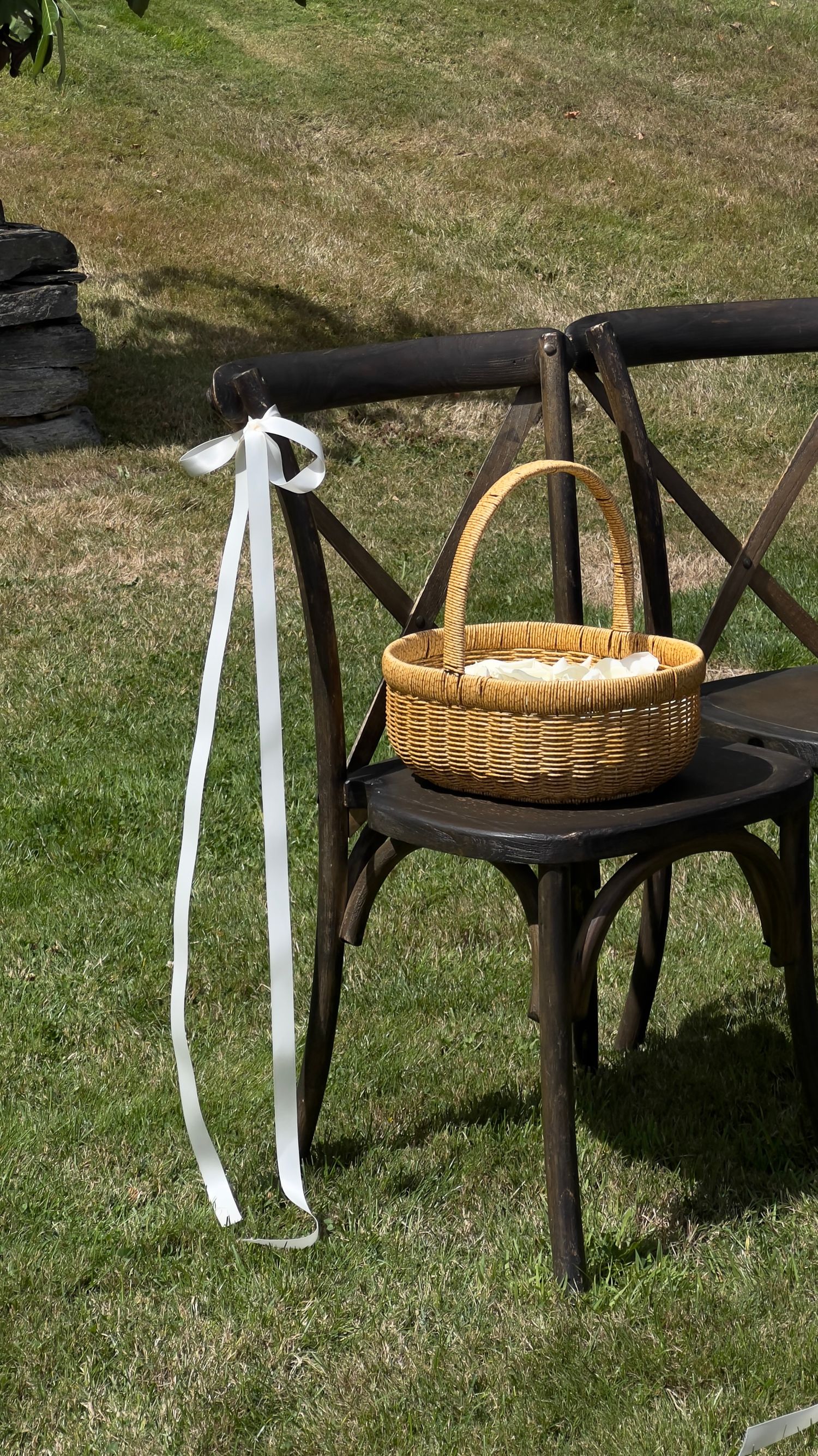 Dark wooden chair with white ribbons and wicker basket set on grass for an outdoor event. content creation in new zealand