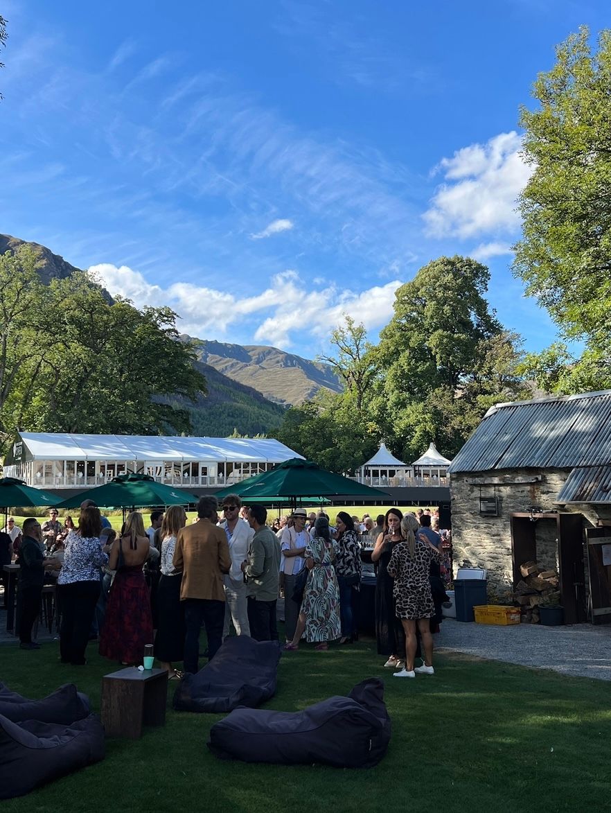 Outdoor garden party with bean bags on lawn and mountain backdrop under blue sky with wispy clouds.
