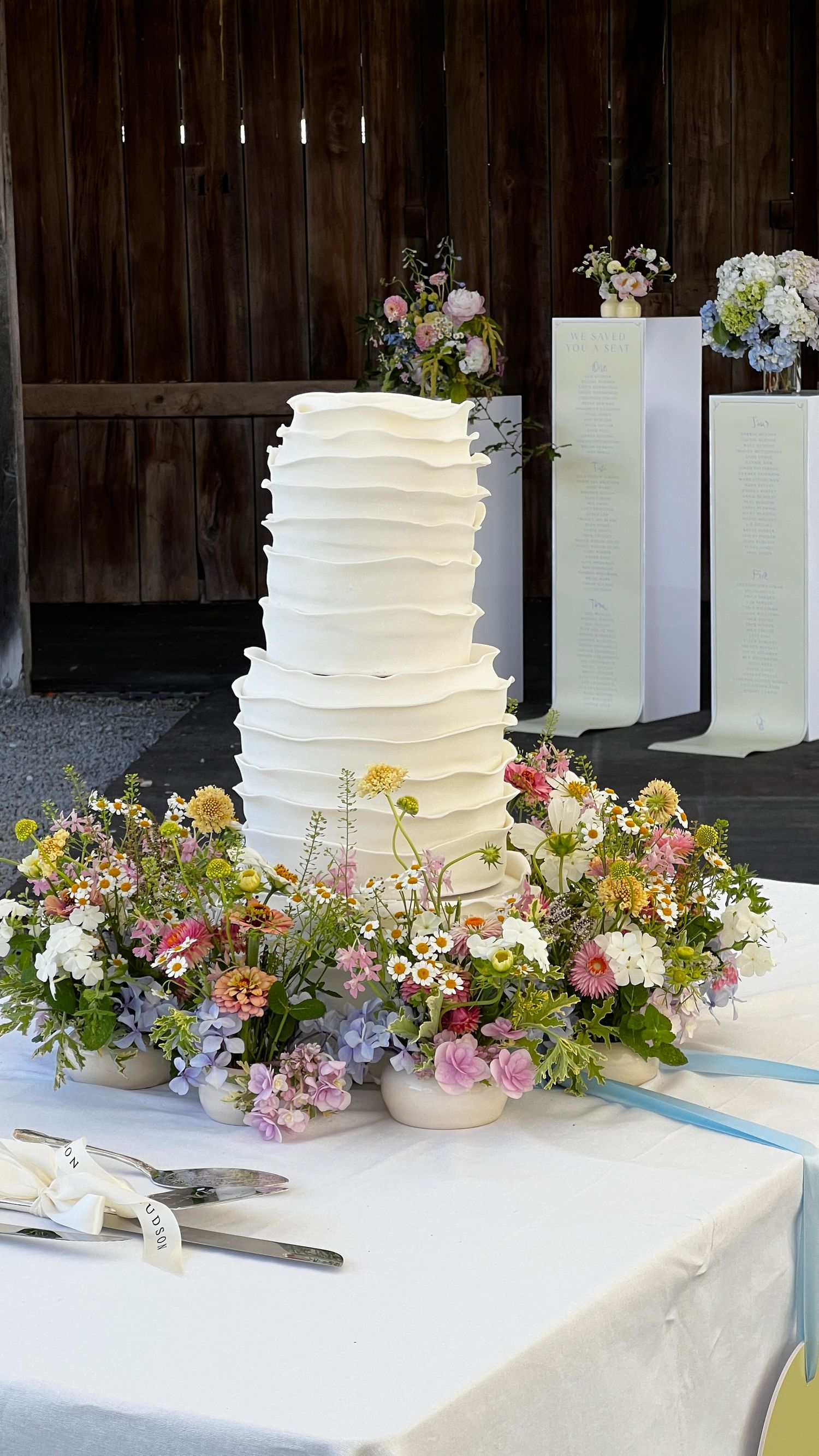 White tiered wedding cake with rustic textured frosting surrounded by vibrant floral decorations. content creation in new zealand