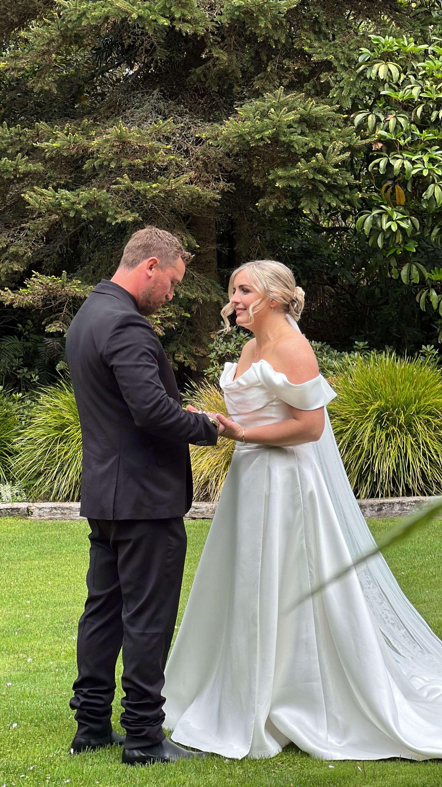A couple in formal attire sharing an intimate moment during their wedding ceremony on a manicured lawn. content creation in new zealand