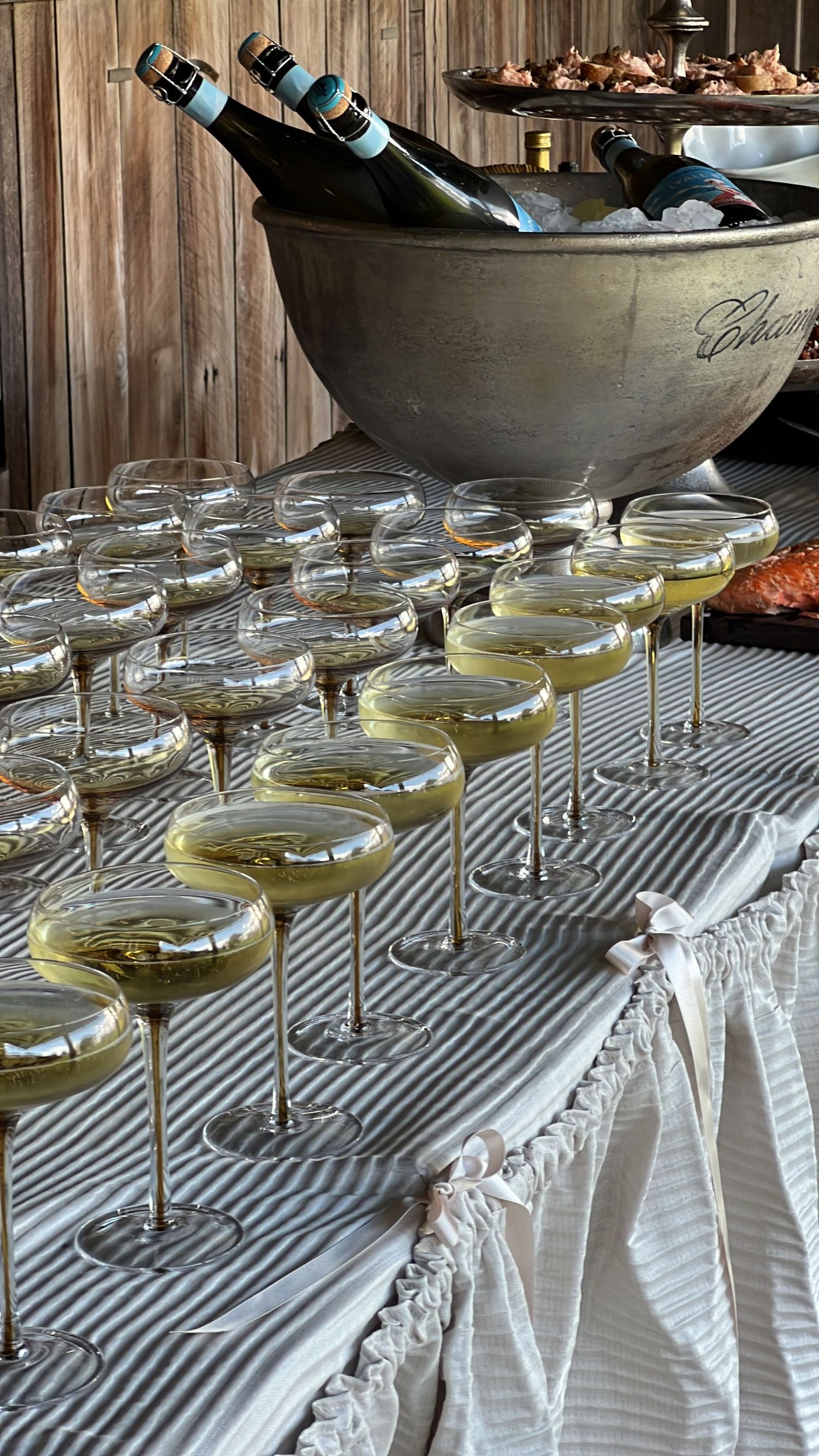 Row of champagne glasses lined up on a striped tablecloth at an elegant event setup.