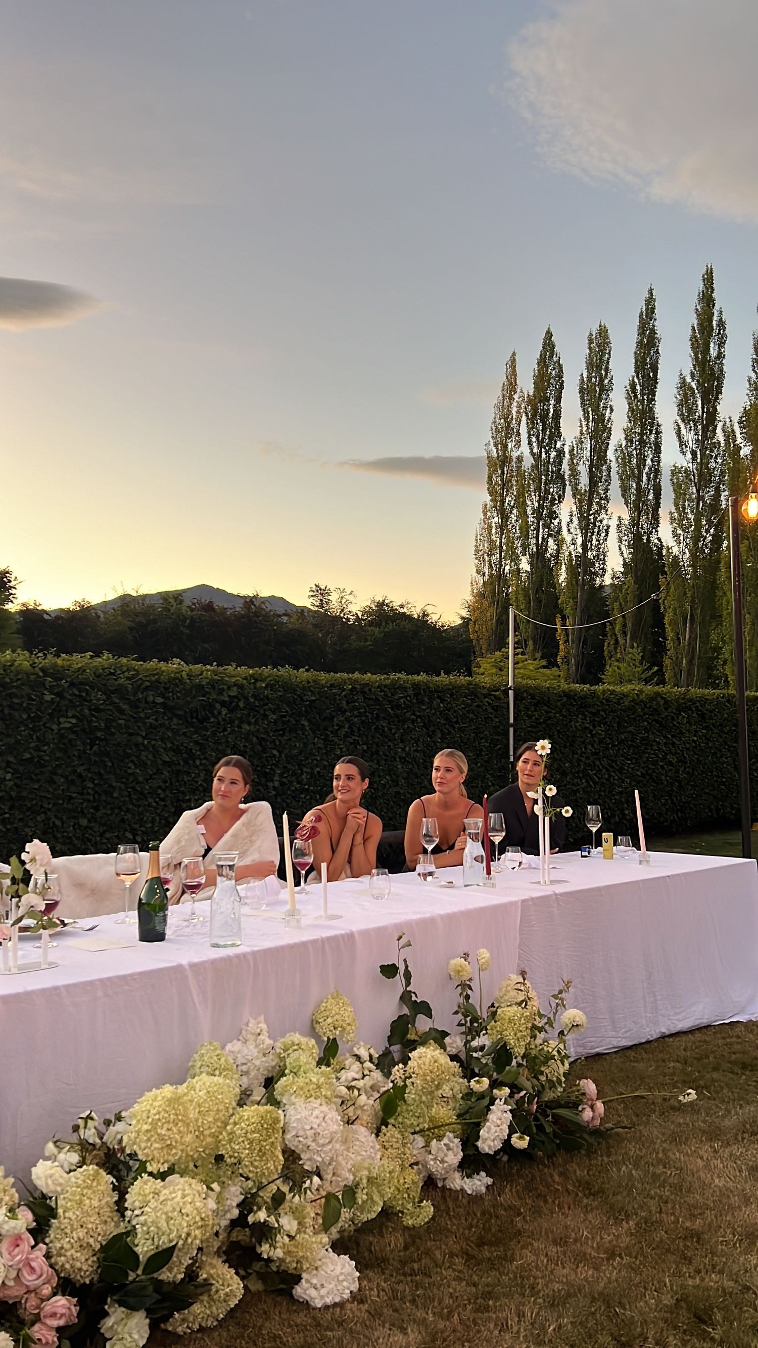Outdoor wedding reception with white hydrangeas decorating long banquet table at sunset. content creation in new zealand
