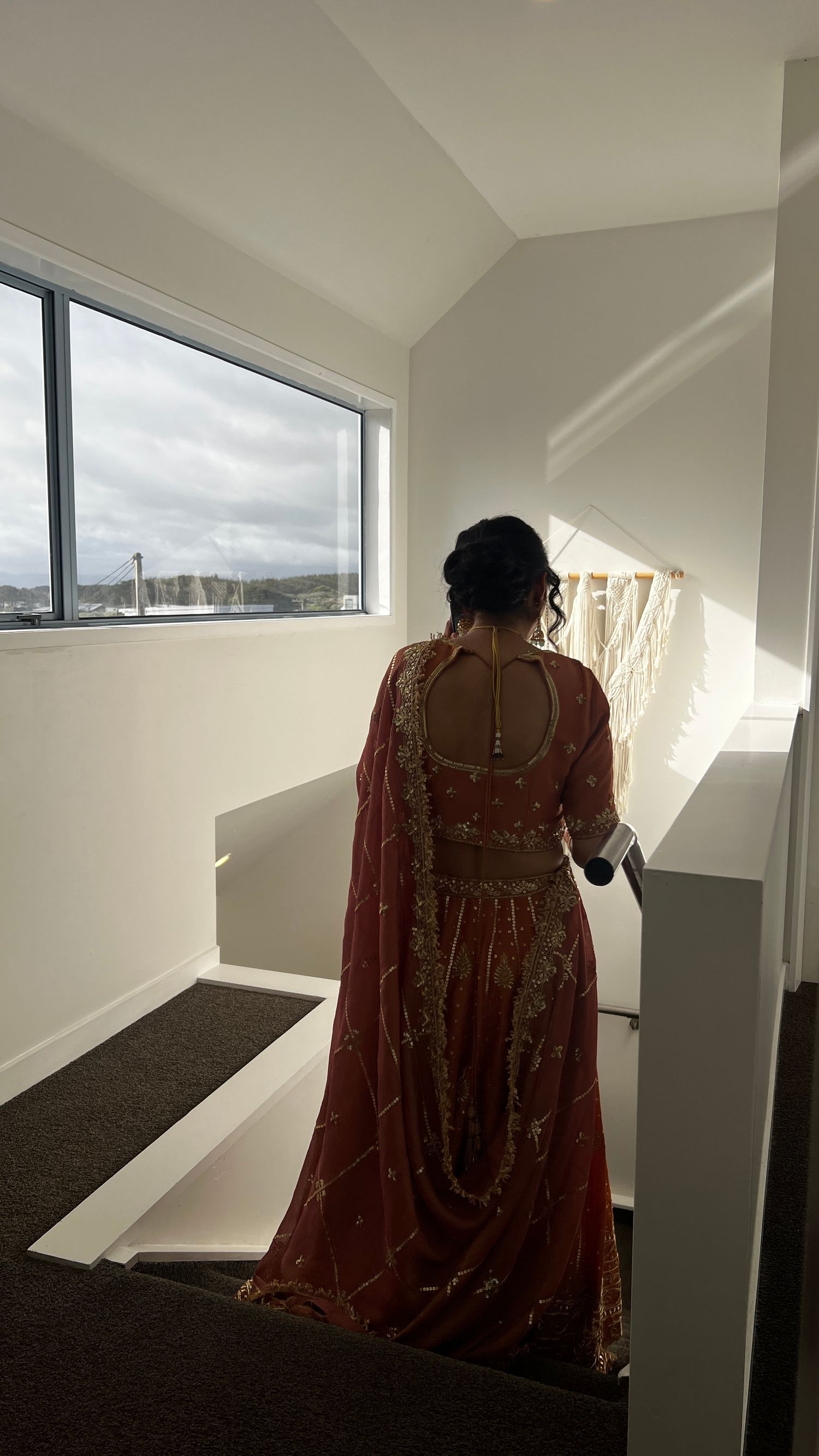 Back view of maroon and gold embroidered lehenga against window with scenic view. indian wedding