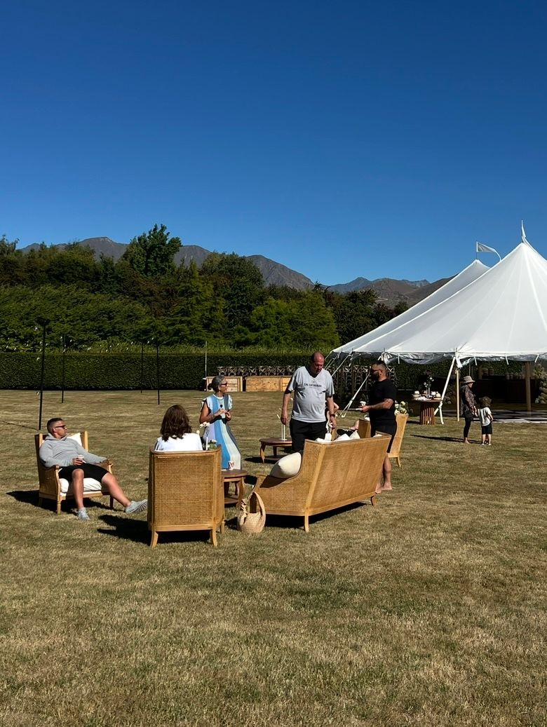 People lounging on outdoor couches arranged in a grassy field with mountains visible in the background.