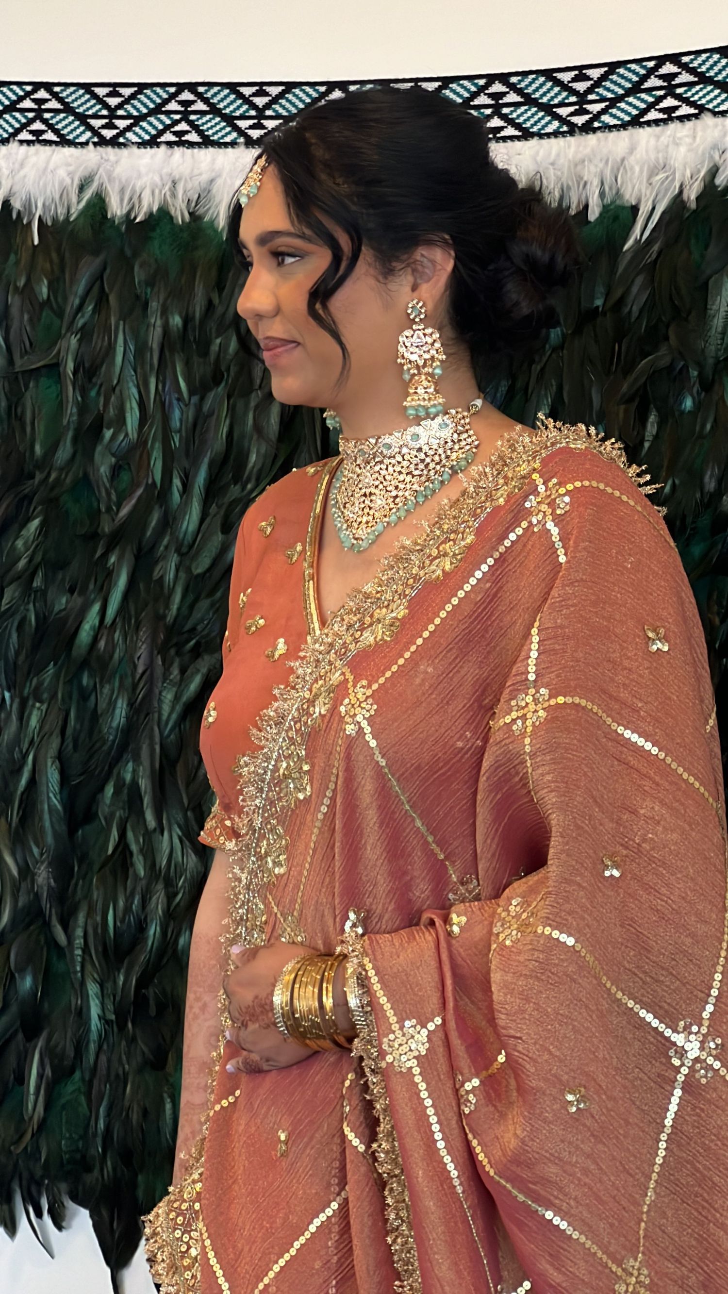 Elegant rust-colored saree with golden embroidery and jewelry details against a dark background.