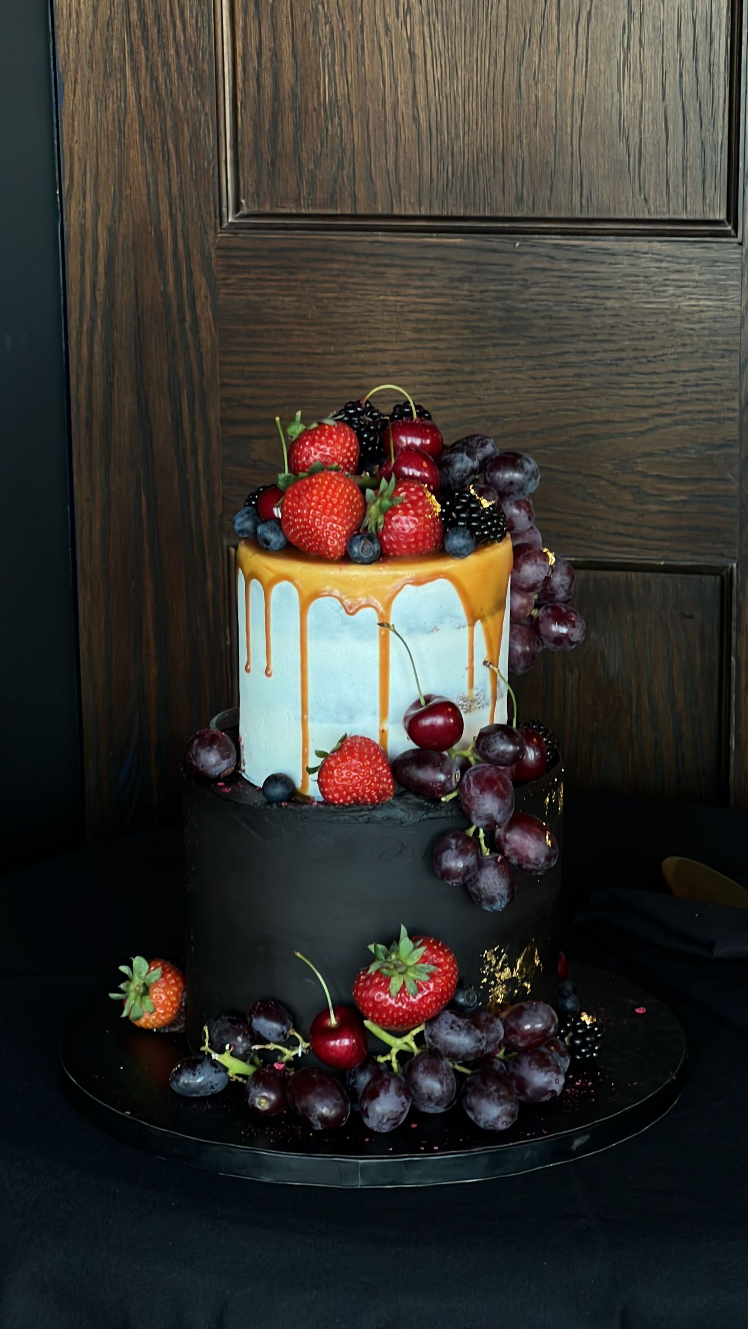 Elegant drip cake decorated with fresh strawberries, cherries and purple flowers.