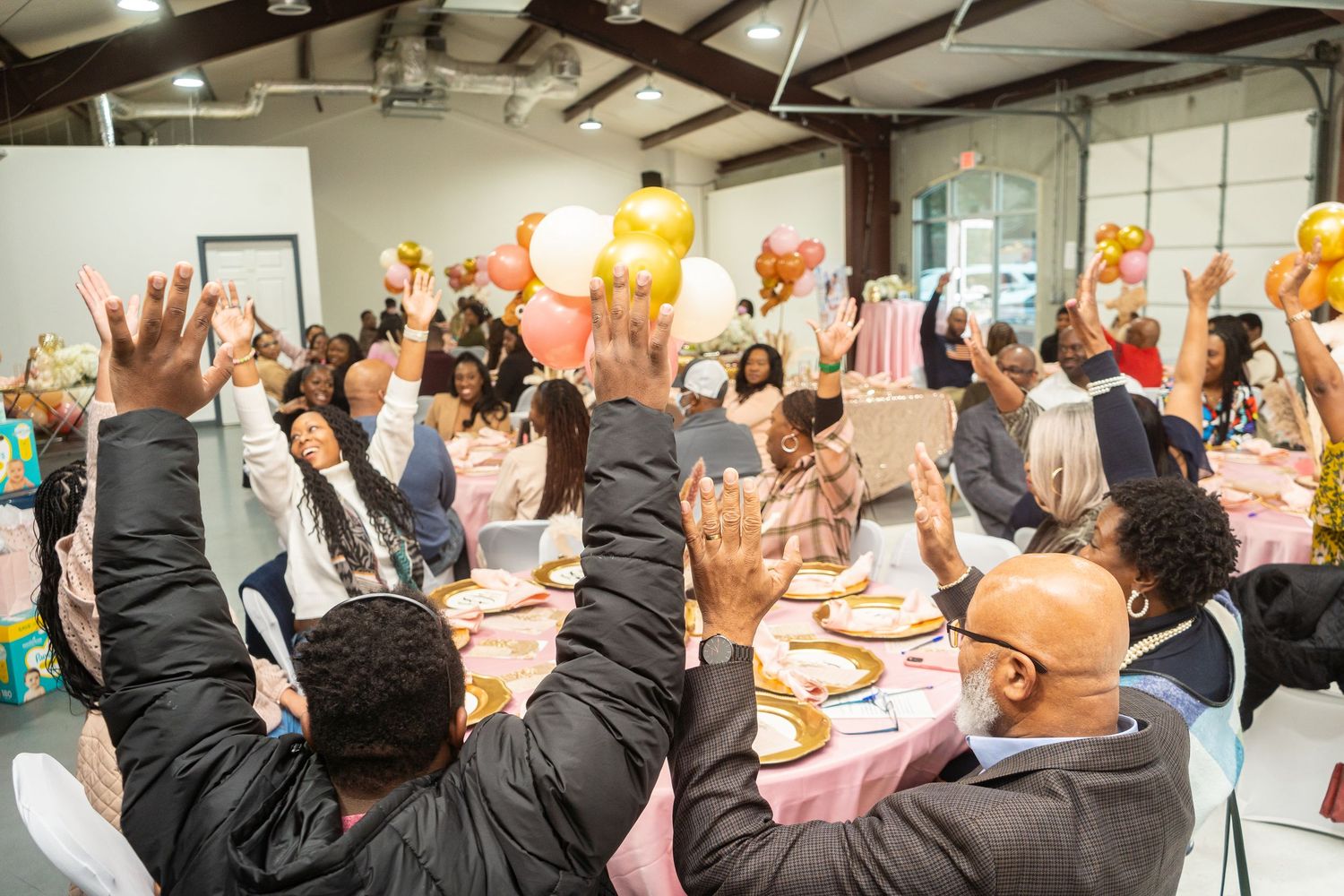 Event photography in Austell, Georgia — guests raising their hands in celebration during a lively baby-shower reception. Captured by Murray