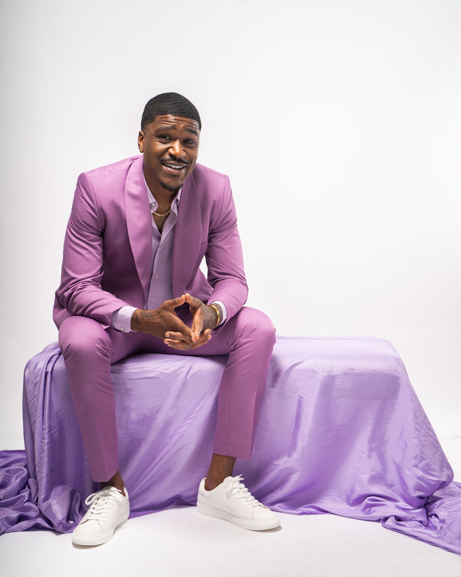 Studio portrait session in Kennesaw, Georgia — confident man in a lavender suit seated on a draped bench with a bright smile and clean white