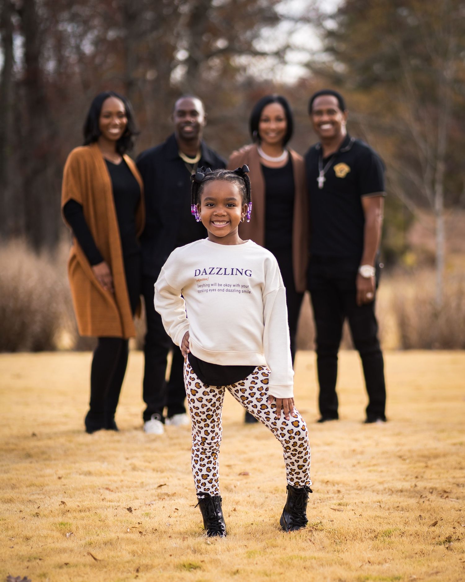 Outdoor family session in Kennesaw, Georgia — young girl posing confidently in the foreground with family smiling behind her in warm golden
