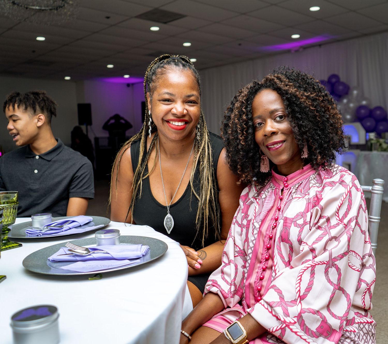 Two black woman smiling at a decorated dinner table in Smyrna, Georgia — captured during a joyful celebration with purple-themed décor