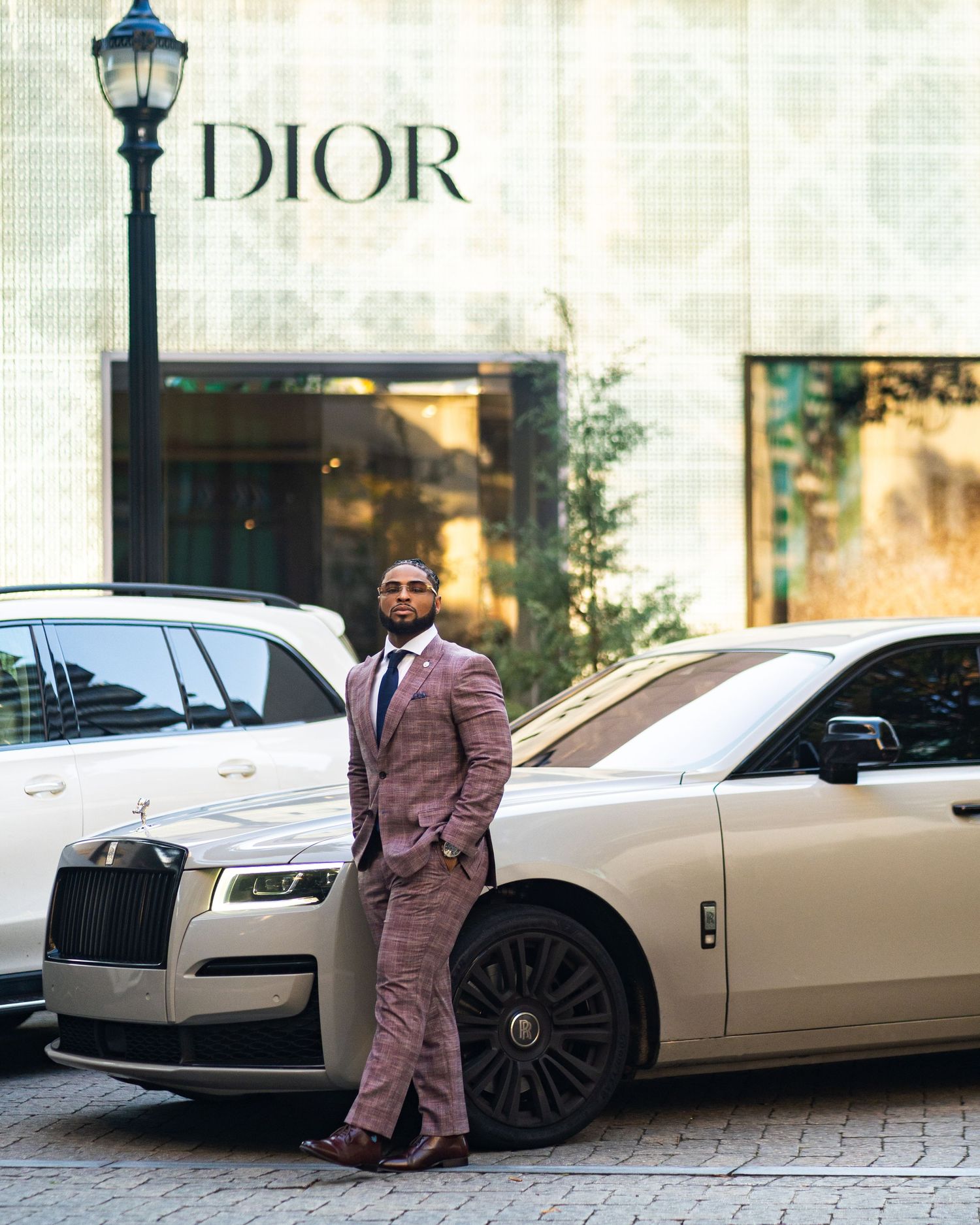 Luxury lifestyle portrait in Buckhead, Atlanta — black man in a tailored suit posing confidently beside a Rolls-Royce and Dior storefront.