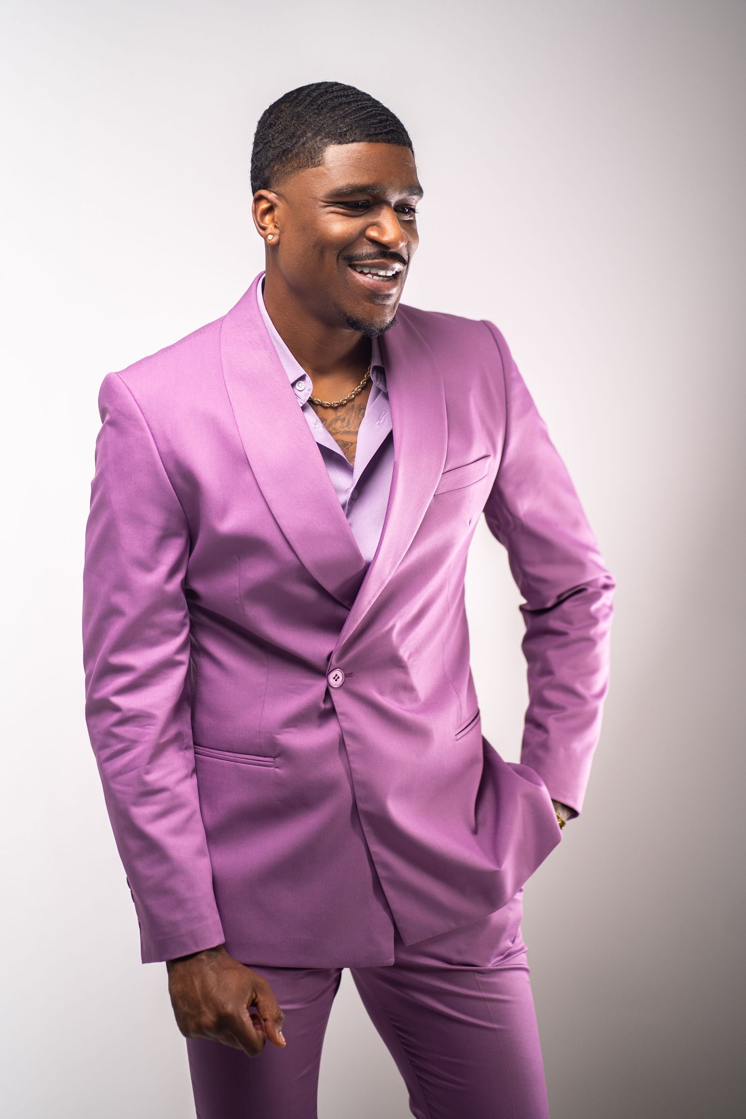 Studio portrait in Marietta, Georgia — stylish black man in lavender suit smiling confidently against a clean white background.