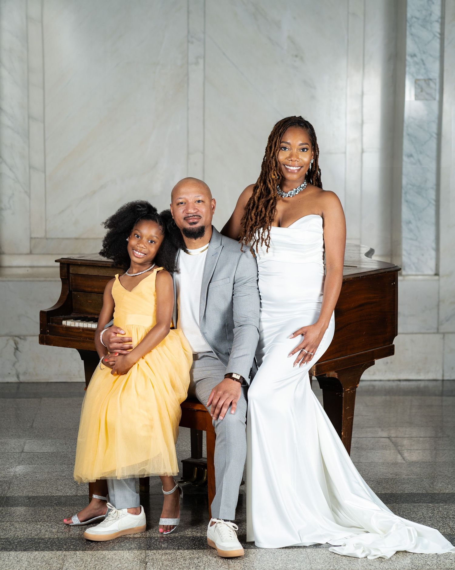 Elegant black family portrait in Vinings, Georgia — mother in a white gown, father in a gray suit, and daughter in a yellow dress