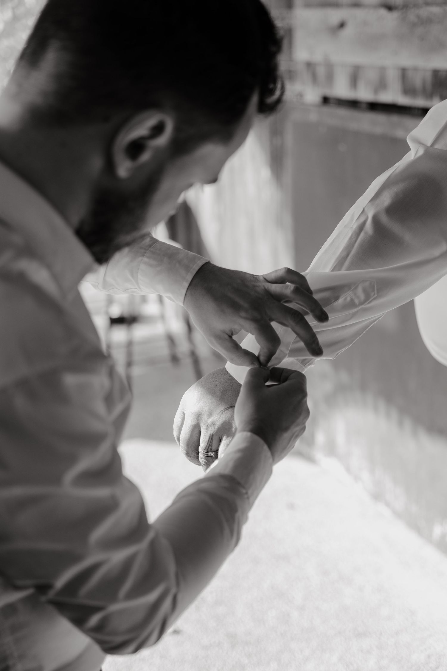 Black and white intimate photo showing hands adjusting a dress sleeve or cuff in a tender moment.