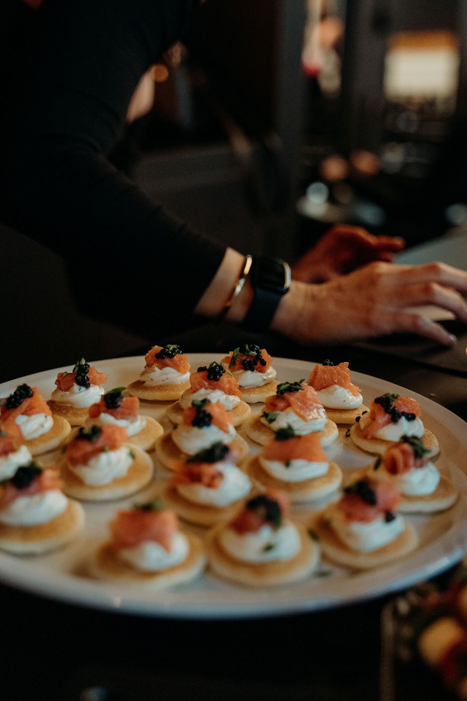 A elegant platter of blinis topped with smoked salmon, cream cheese, and caviar served at an upscale event.