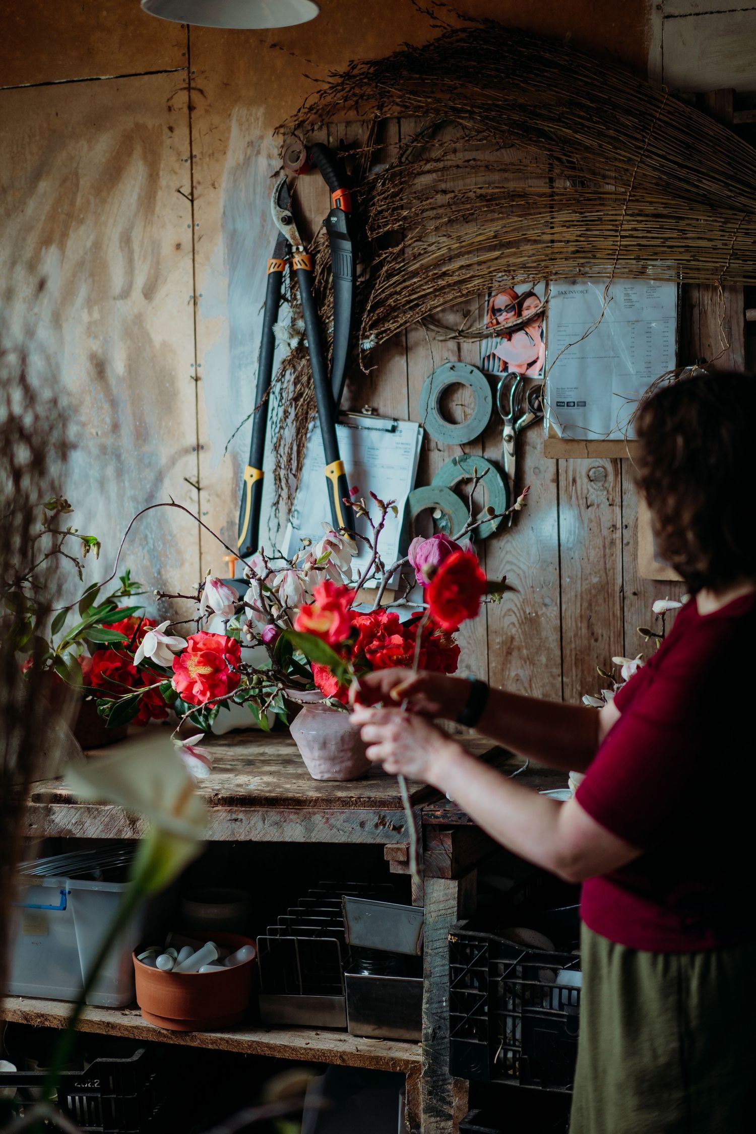 A series of photos showing someone arranging red flowers and greenery in a rustic interior setting with weathered walls.