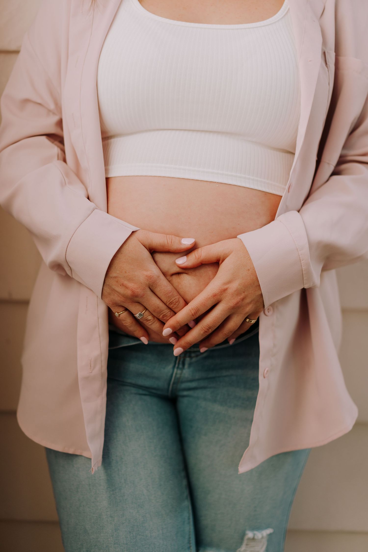 Close-up of hands resting on stomach wearing pink blazer and white crop top.