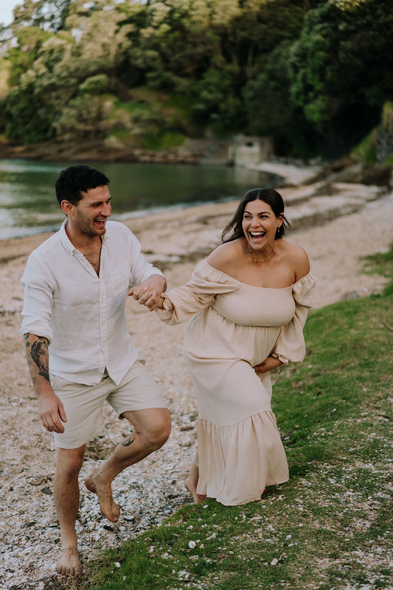 Joyful couple laughing while walking barefoot along a scenic beach pathway.