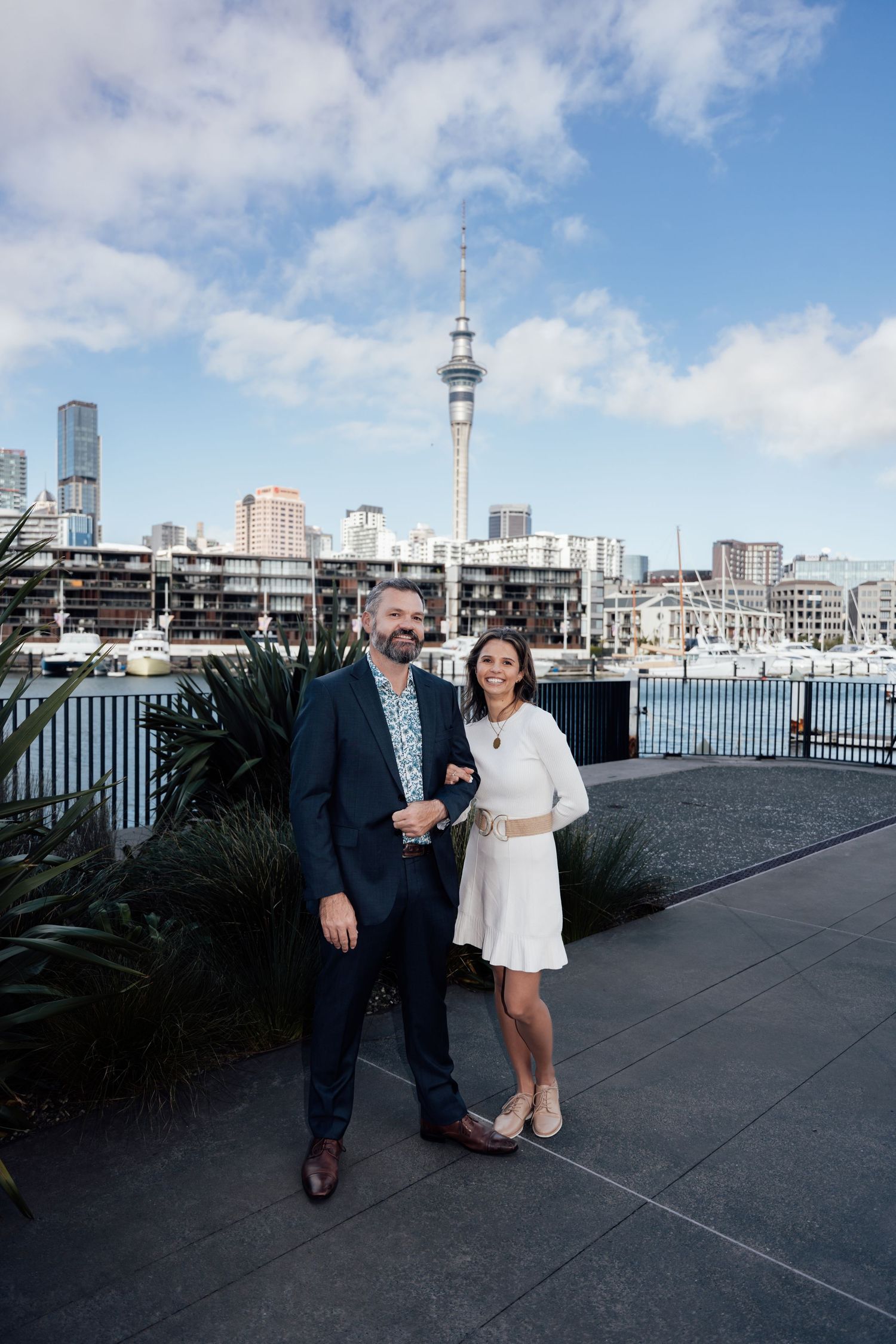 Couple posing in front of Auckland's Viaduct Harbour with Sky Tower and marina in the background.
